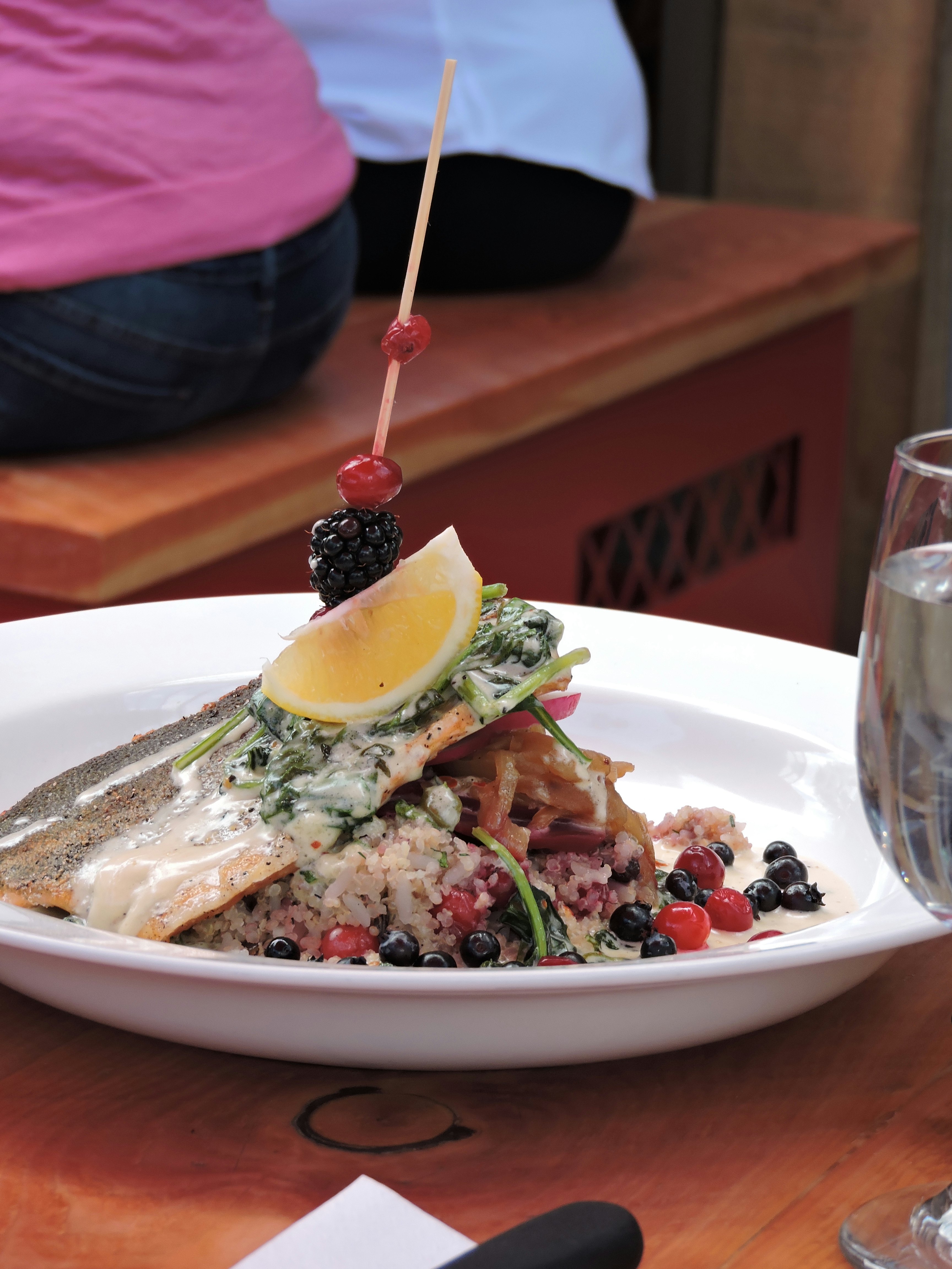 A piece of salmon, pierced by a wooden stick with a lemon slice and berries, lies in a bed of rice mixed with berries; Indigenous food