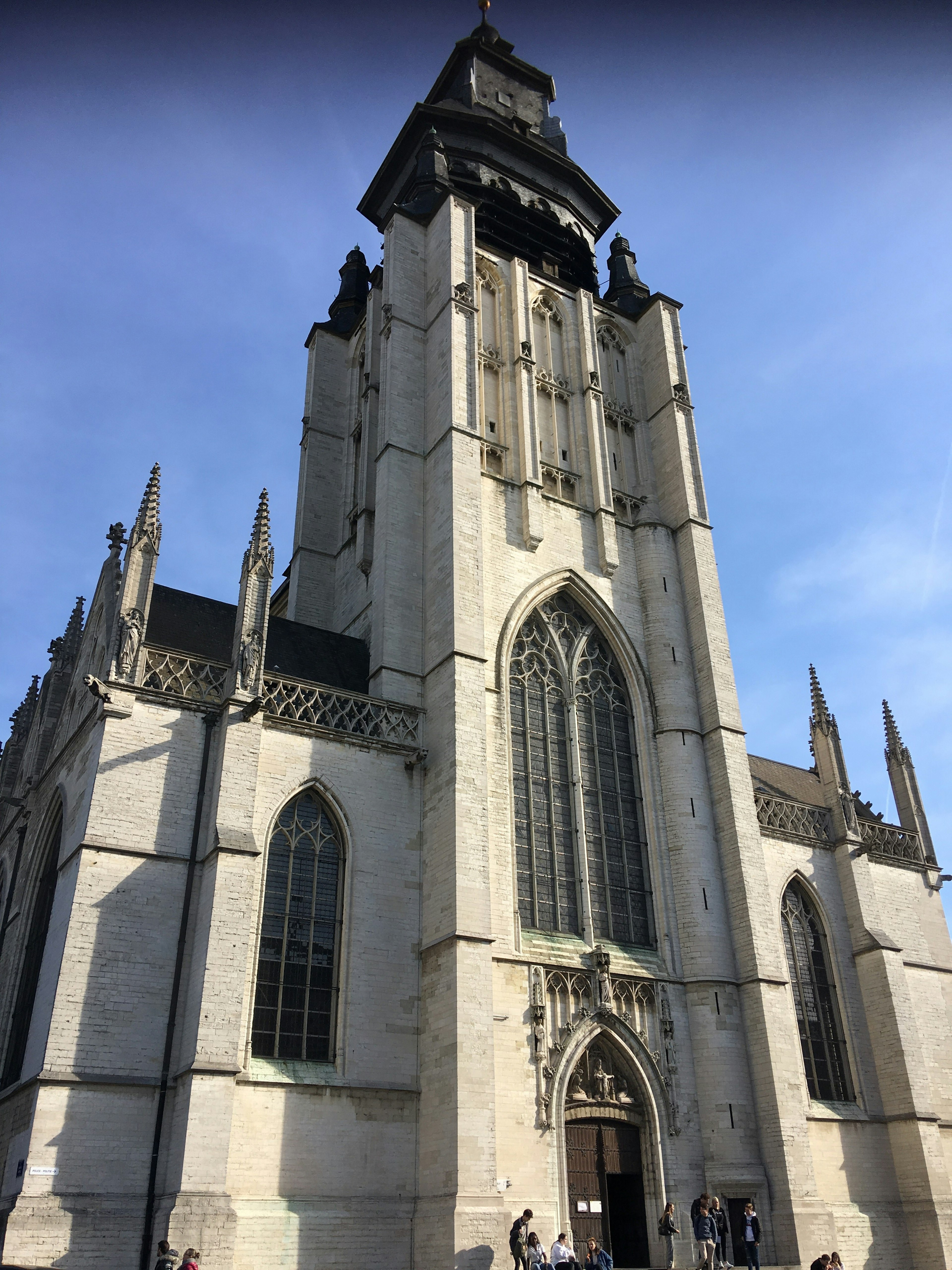 A Gothic church with a tall central tower, spires and arched windows stretches up to a bright blue sky.