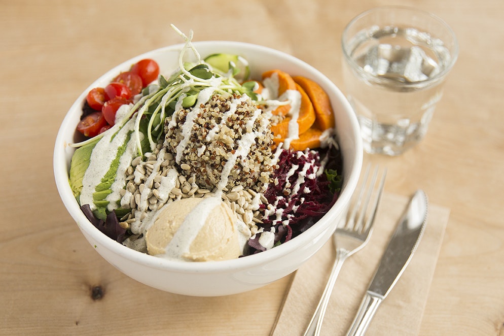 A bowl filled with quinoa, avocado, sweet potatoes, tomatoes and red cabbage sits next to a glass of water and a fork and knife; vegan restaurants San Francisco Bay Area