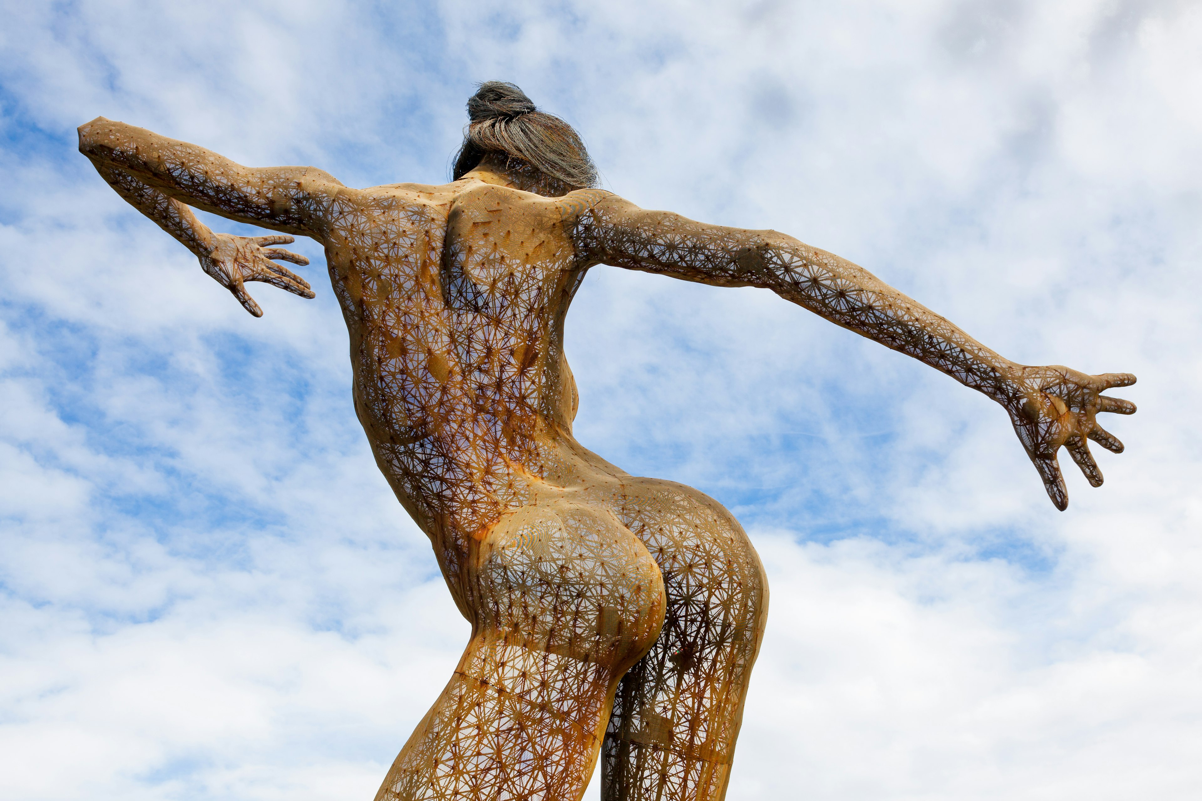 A large mesh sculpture in the form of a woman stands 40-feet high with her arms spread wide apart