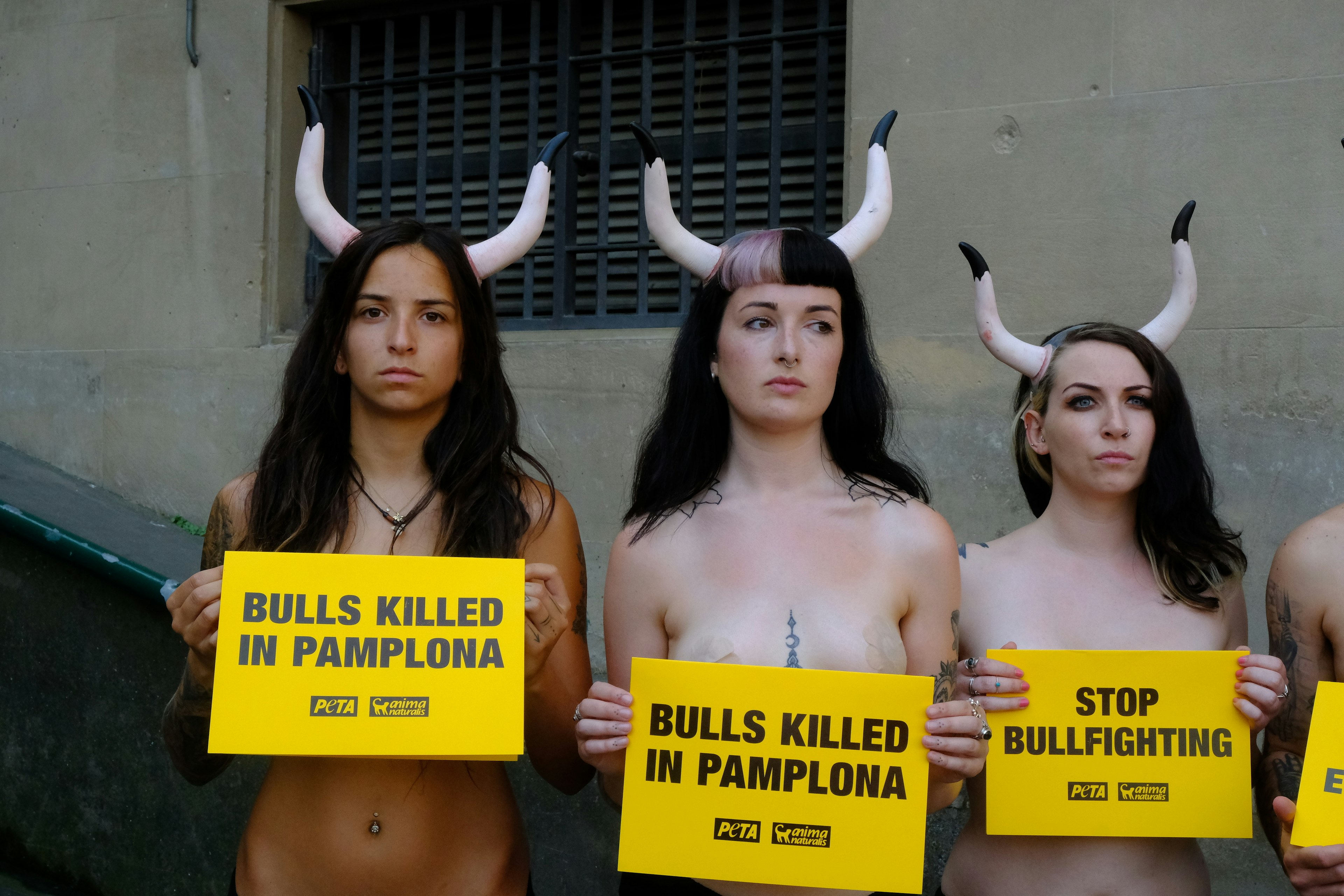 A trio of topless woman wearing bull horns hold signs over their chests that call for the end of bullfighting