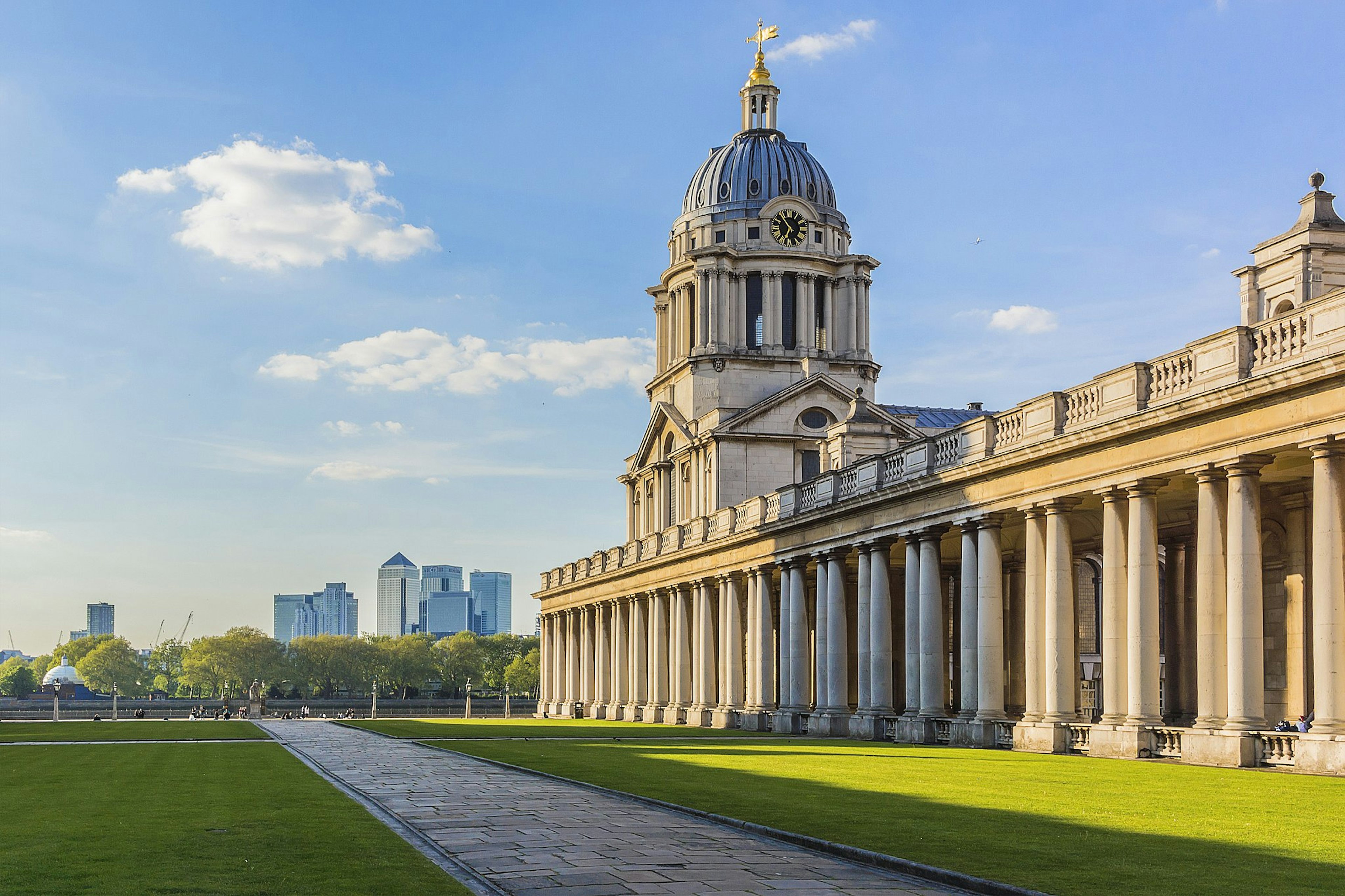 The domed baroque Old Royal Naval College in Greenwich, with a large lawn in front and the modern skyscrapers of Canary Wharf in the distance beyond.