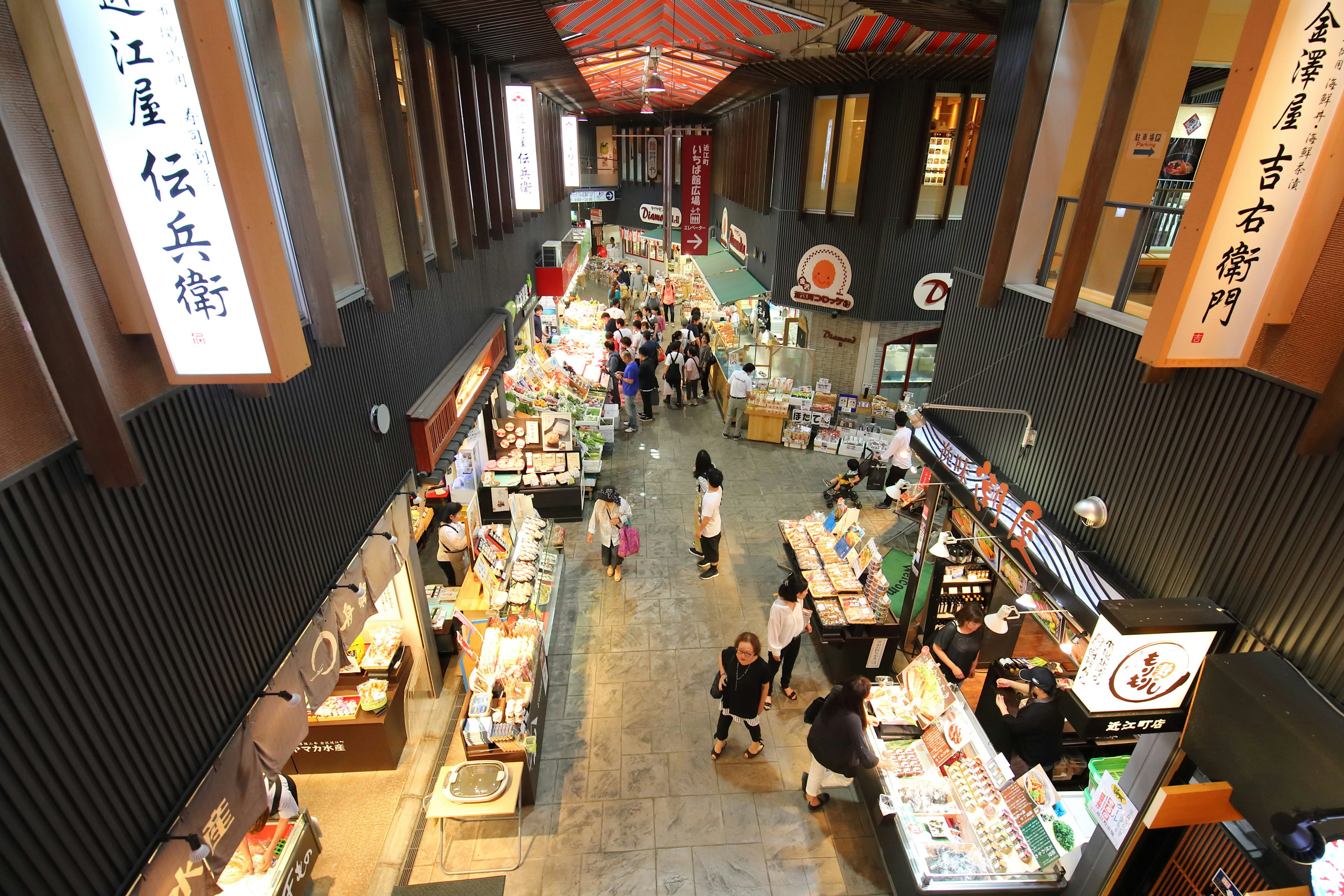 An aerial view of Omicho fish market with shoppers browsing stalls filled with fish and other goods.