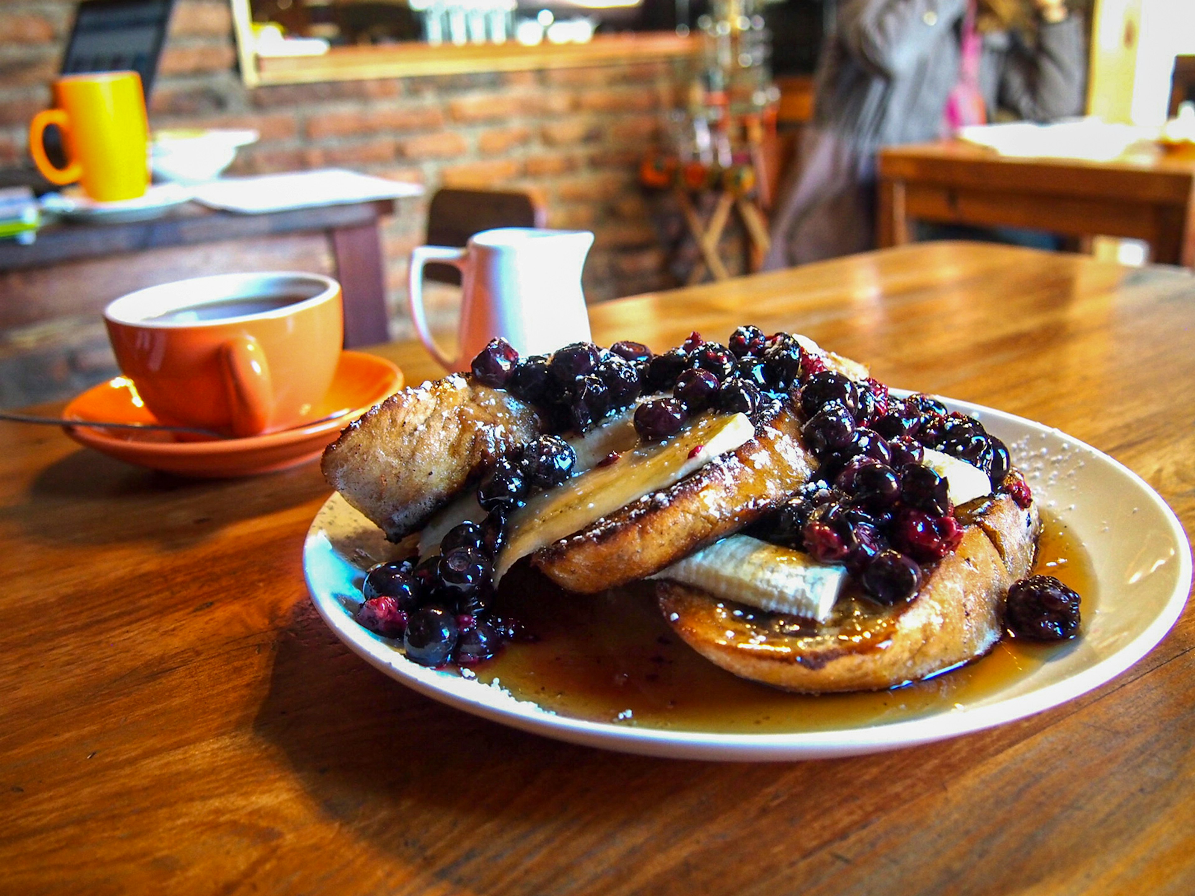 A plate with french toast topped with bananas and blueberries, with a cup of coffee in the background. Santiago, Chile.