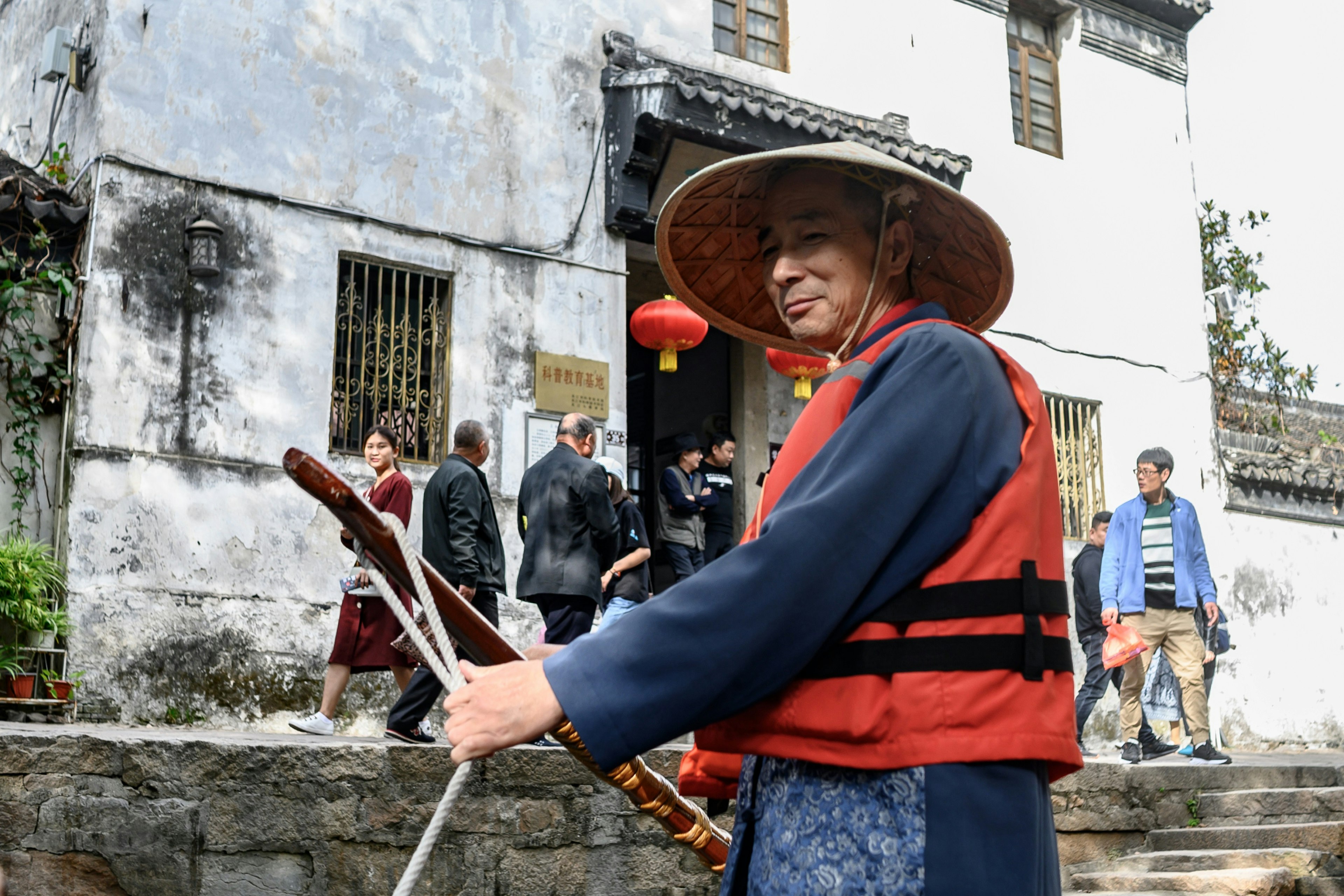 A man steers a boat along a Suzhou canal while wearing a bright orange life jacket.