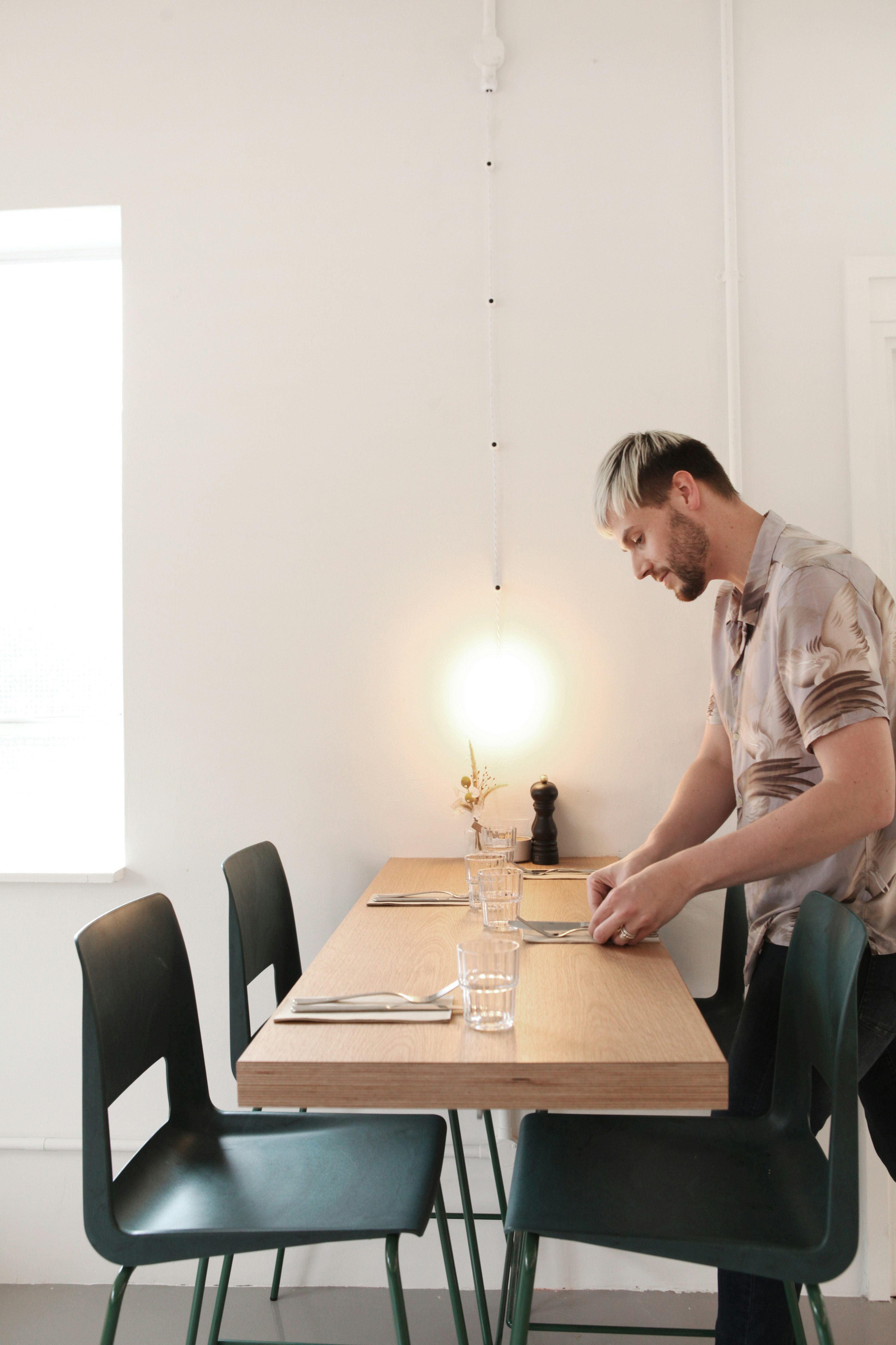 A member of staff at Ozone in east London sets a wooden table with black chairs and a white wall behind it.