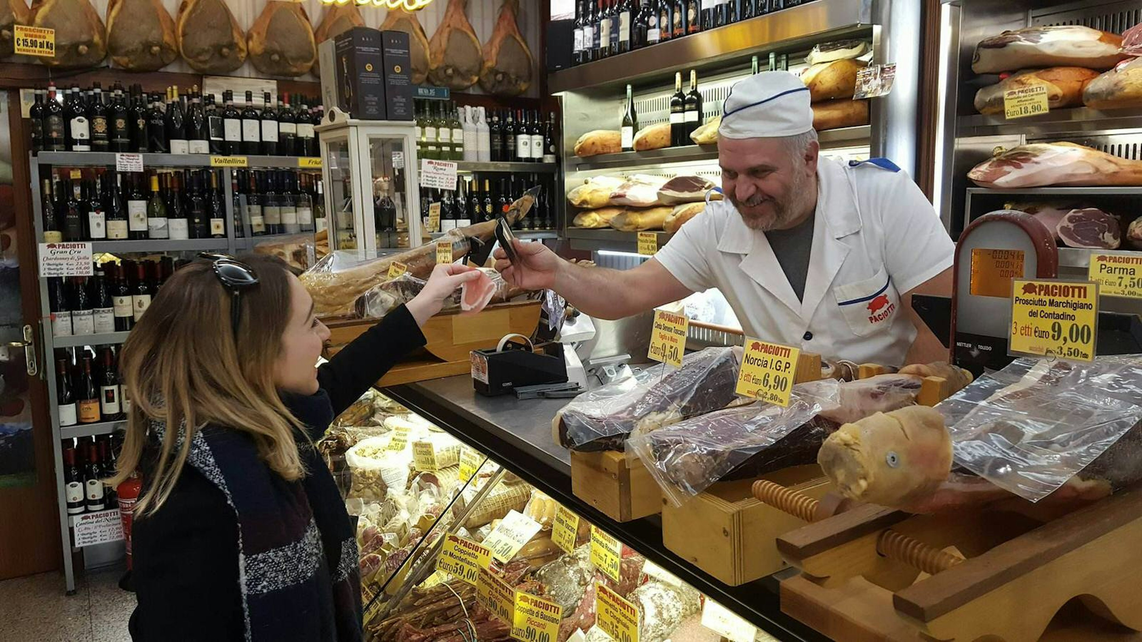 The writer, Alexandra Bruzzese, takes a slice of prosciutto ham from the proprietor at Paciotti Salumeria