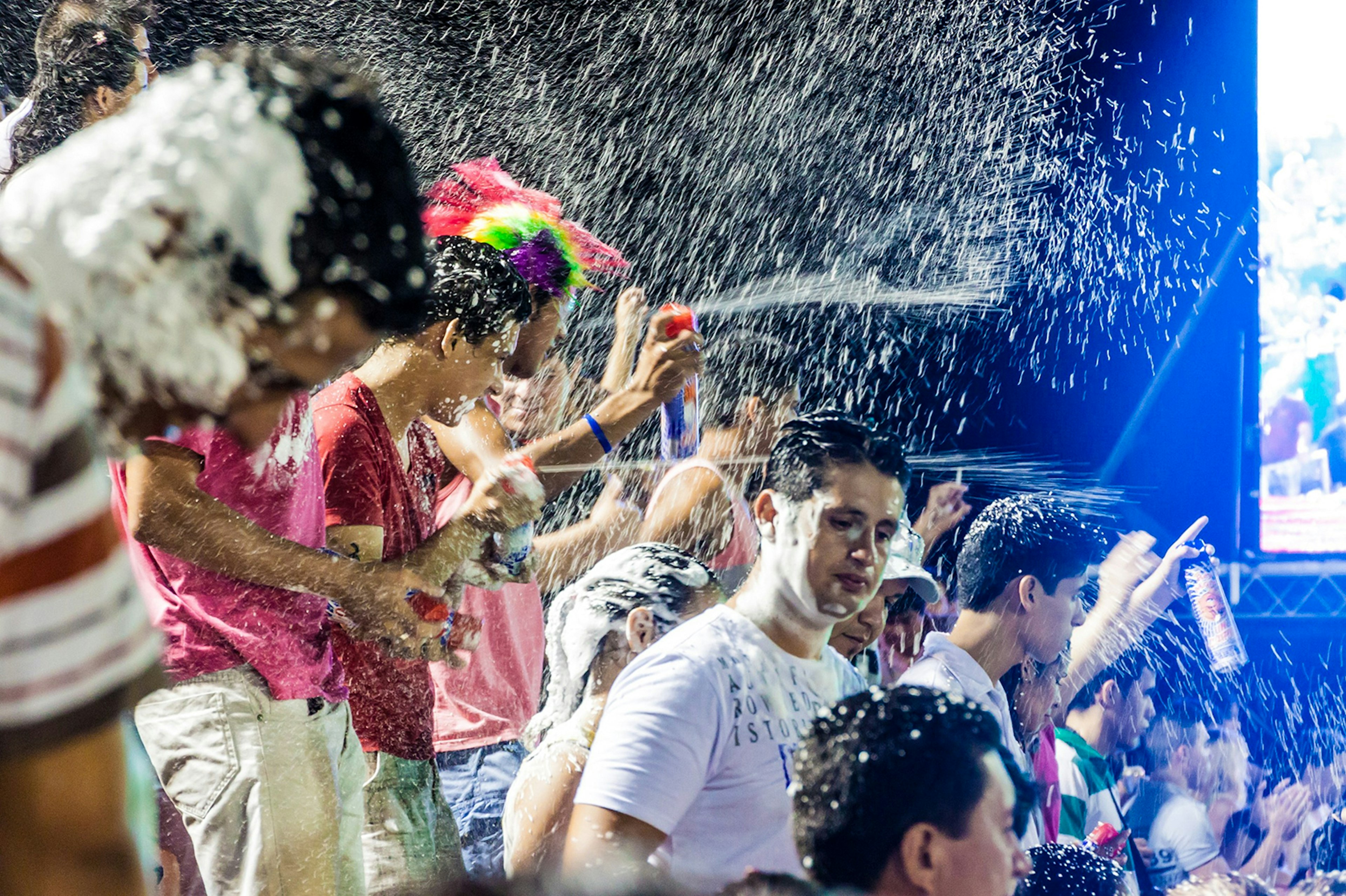 A group of people spray cans of fake snow in the air, covering those nearby