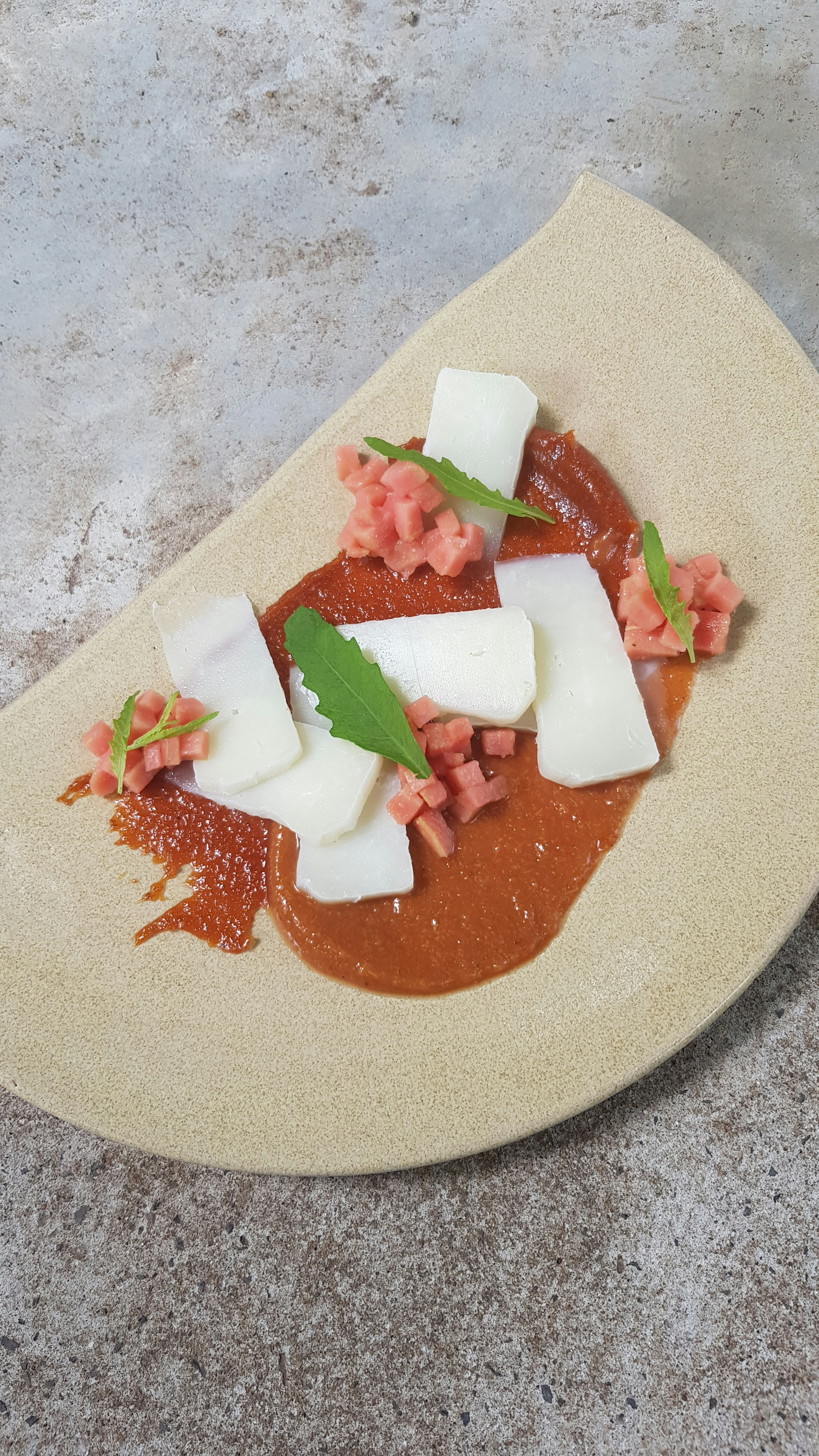 small pieces of candied papaya are placed in small piles around a smear or pureed fruit that is topped with thin slices of Paraguyan cheese