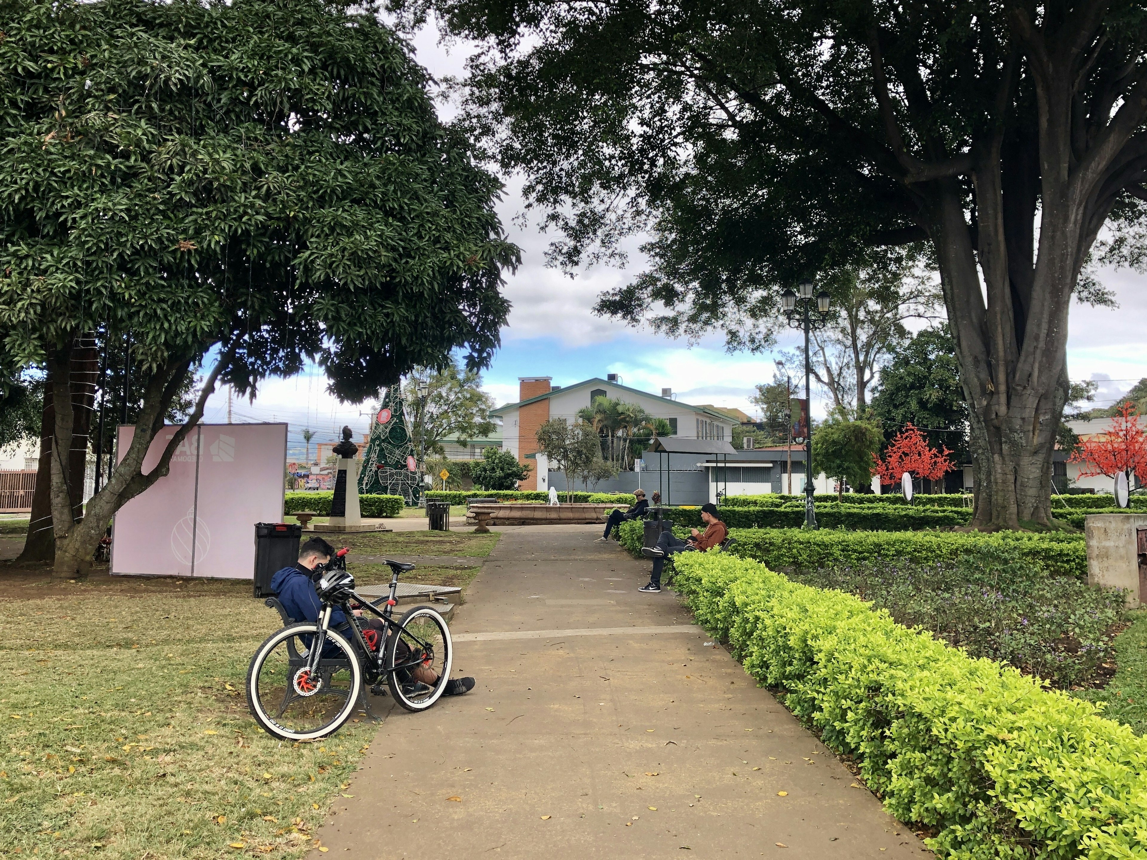 A group of people relax on park benches in a small city park in Barrio Escalante.