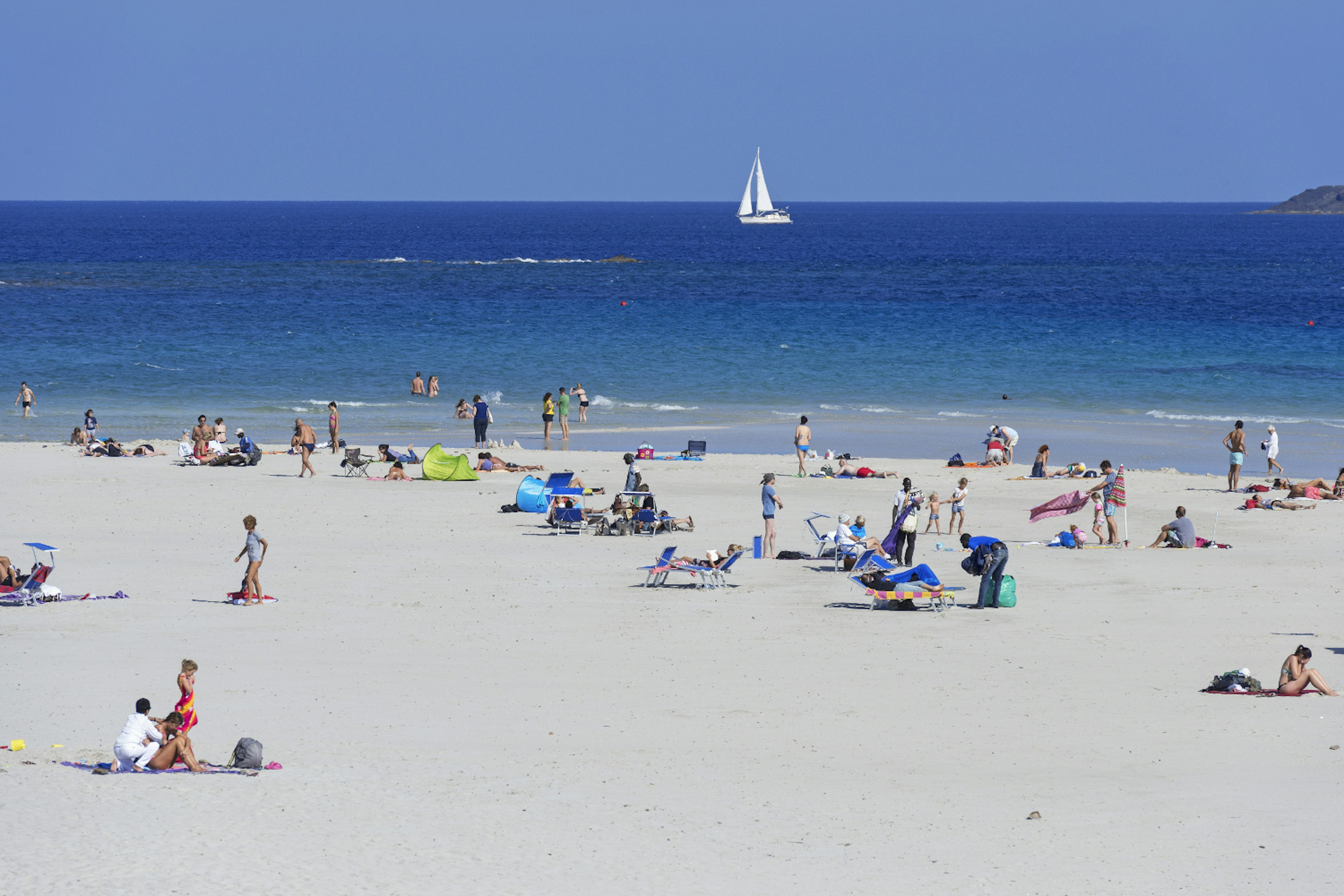 A crowd of beachgoers relax on the white sands of Spiaggia della Pelosa in Stintino, Sardinia.