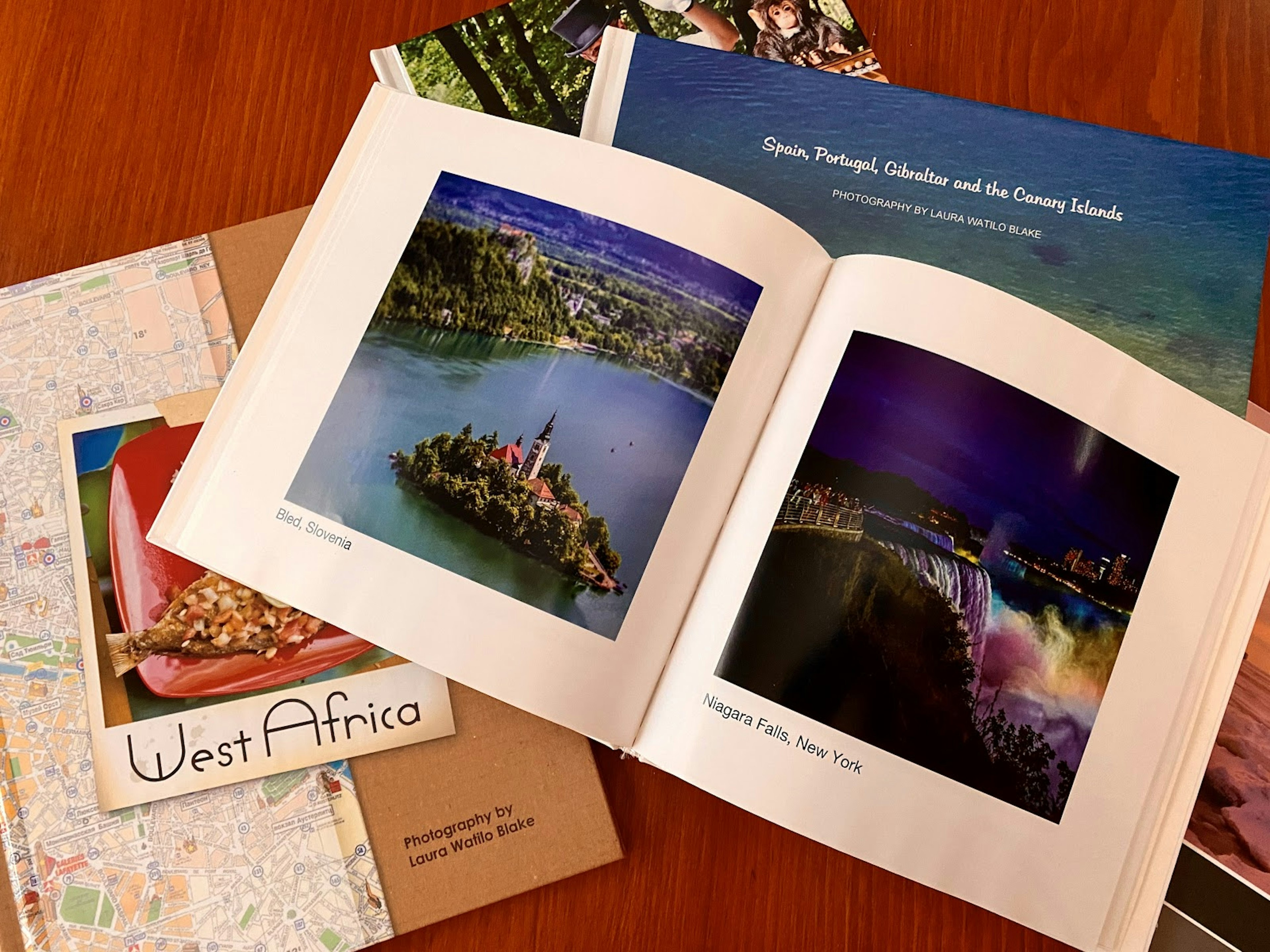 A photo book overlays several other travel documents, including a map, a postcard from West Africa, and two other books