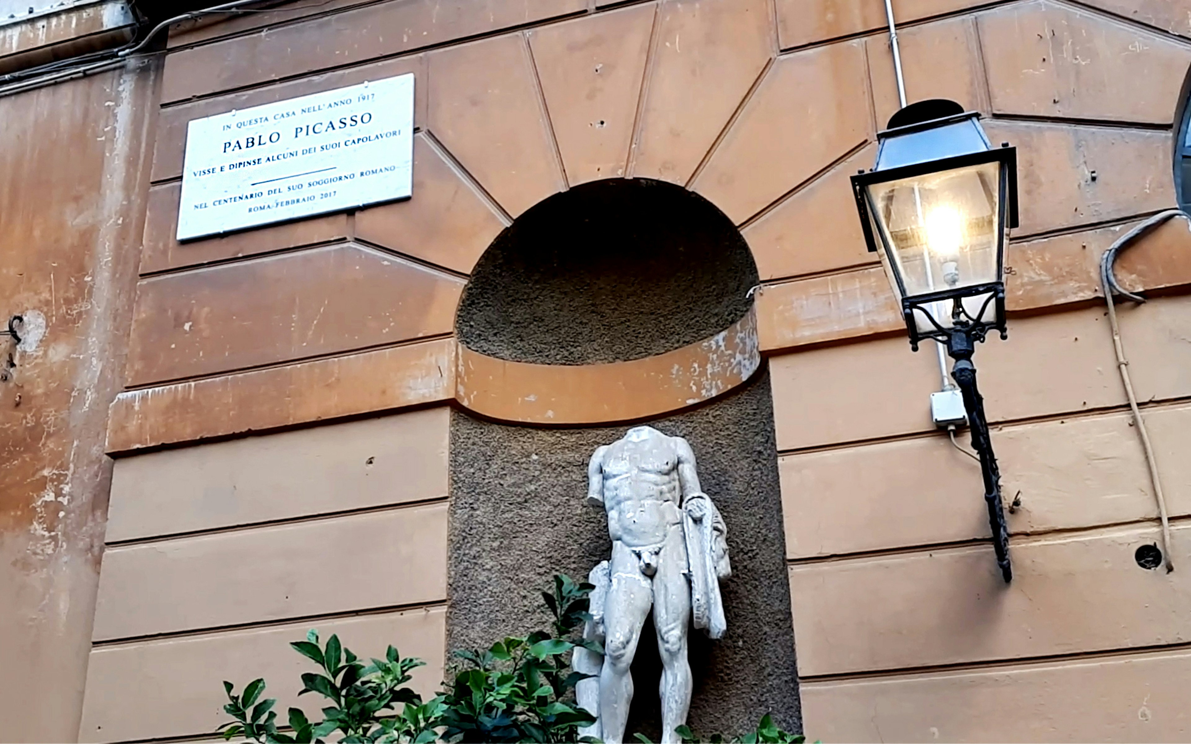 A sign marks the home of Pablo Picasso, positioned on the building above and to the left of an alcove with a statue of a headless nude statue