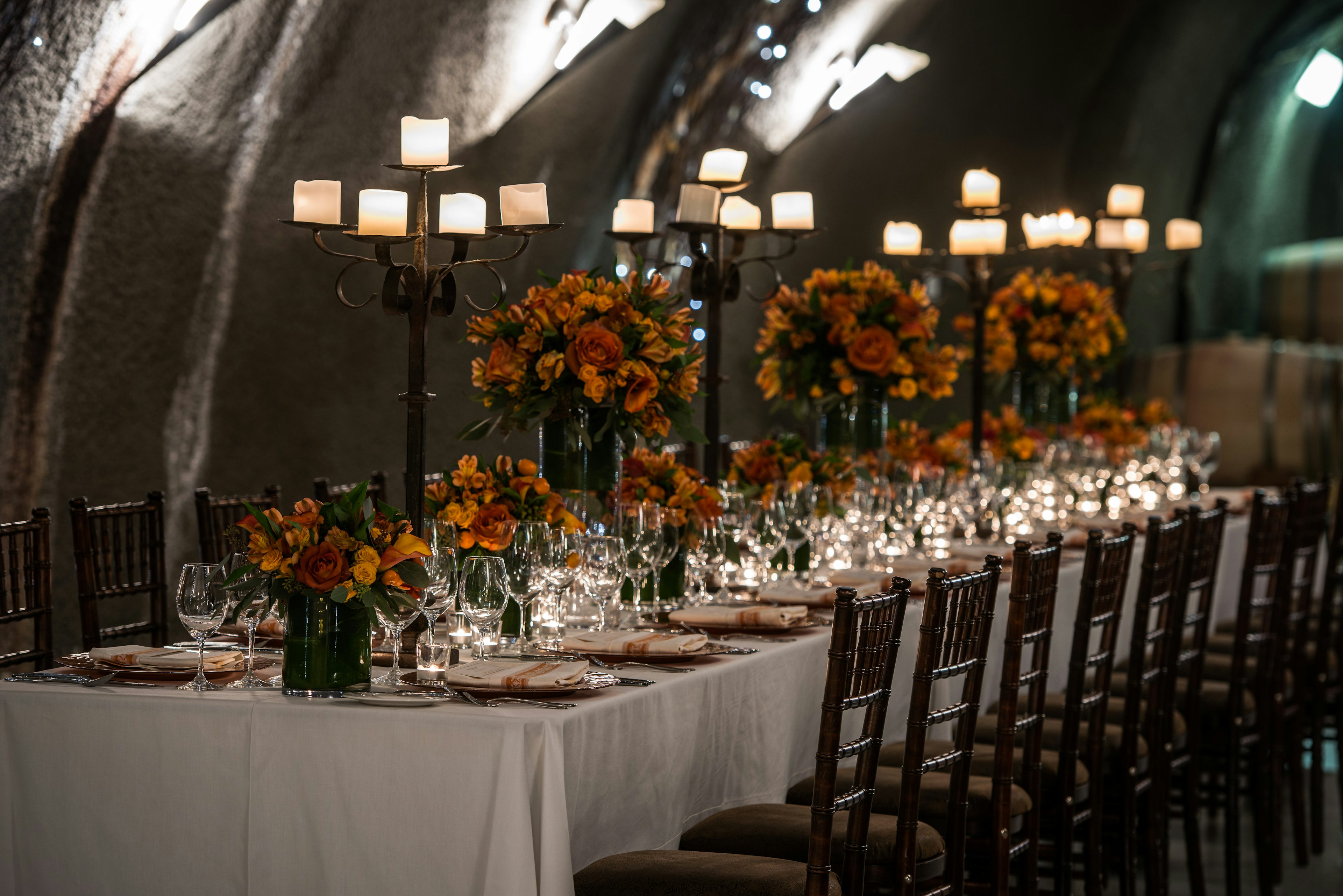 A long table set with candelabra an orange flowers is prepared for an elegant meal