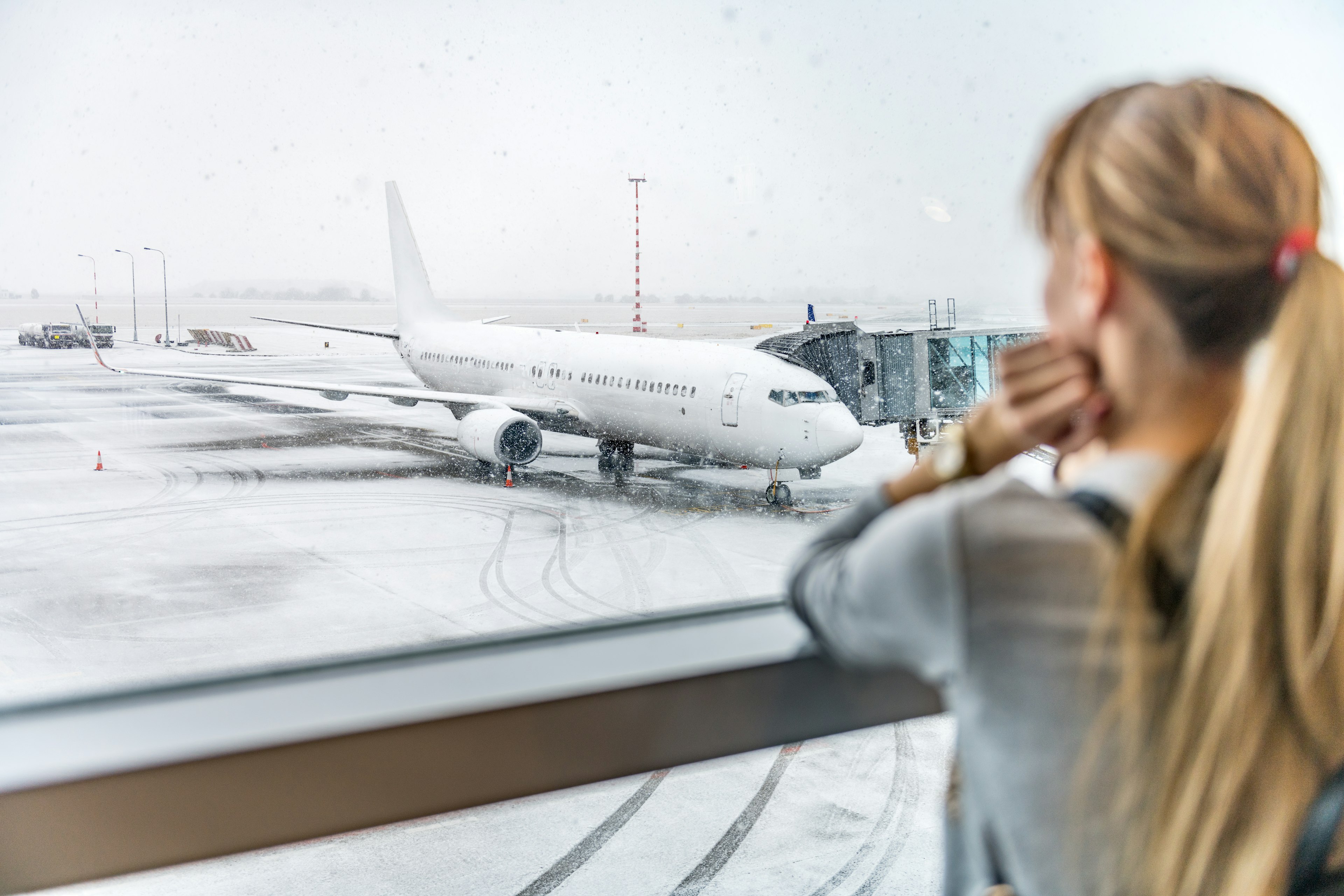 A woman stares on through a window as a plane sits in the snow