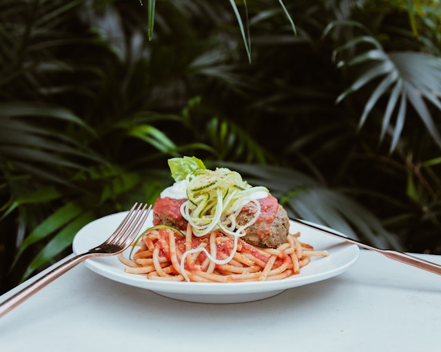A fork and knife sit on opposite sides of a white plate filled with vegan spaghetti and faux meatballs; vegan restaurants Miami