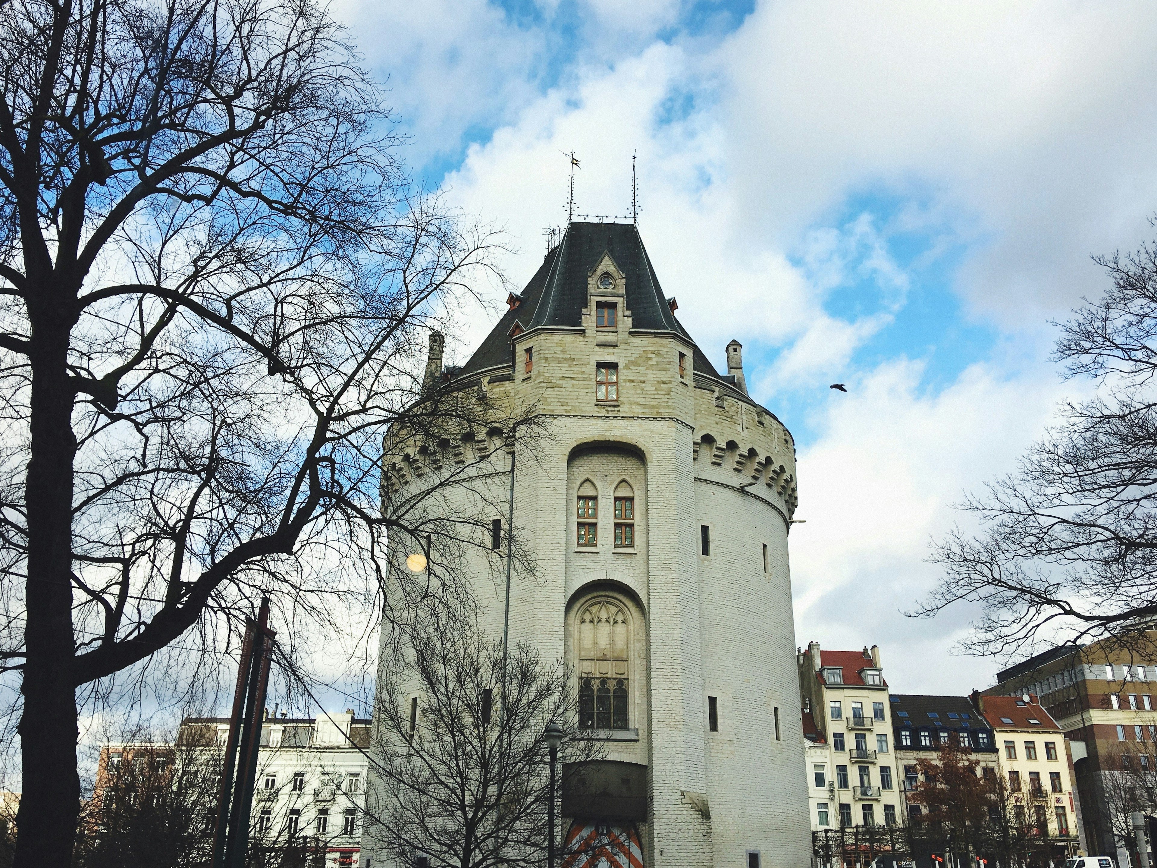 A gatehouse tower embellished with windows and neo-Gothic turrets; there are bare trees next to the tower and tall terraced houses beyond.