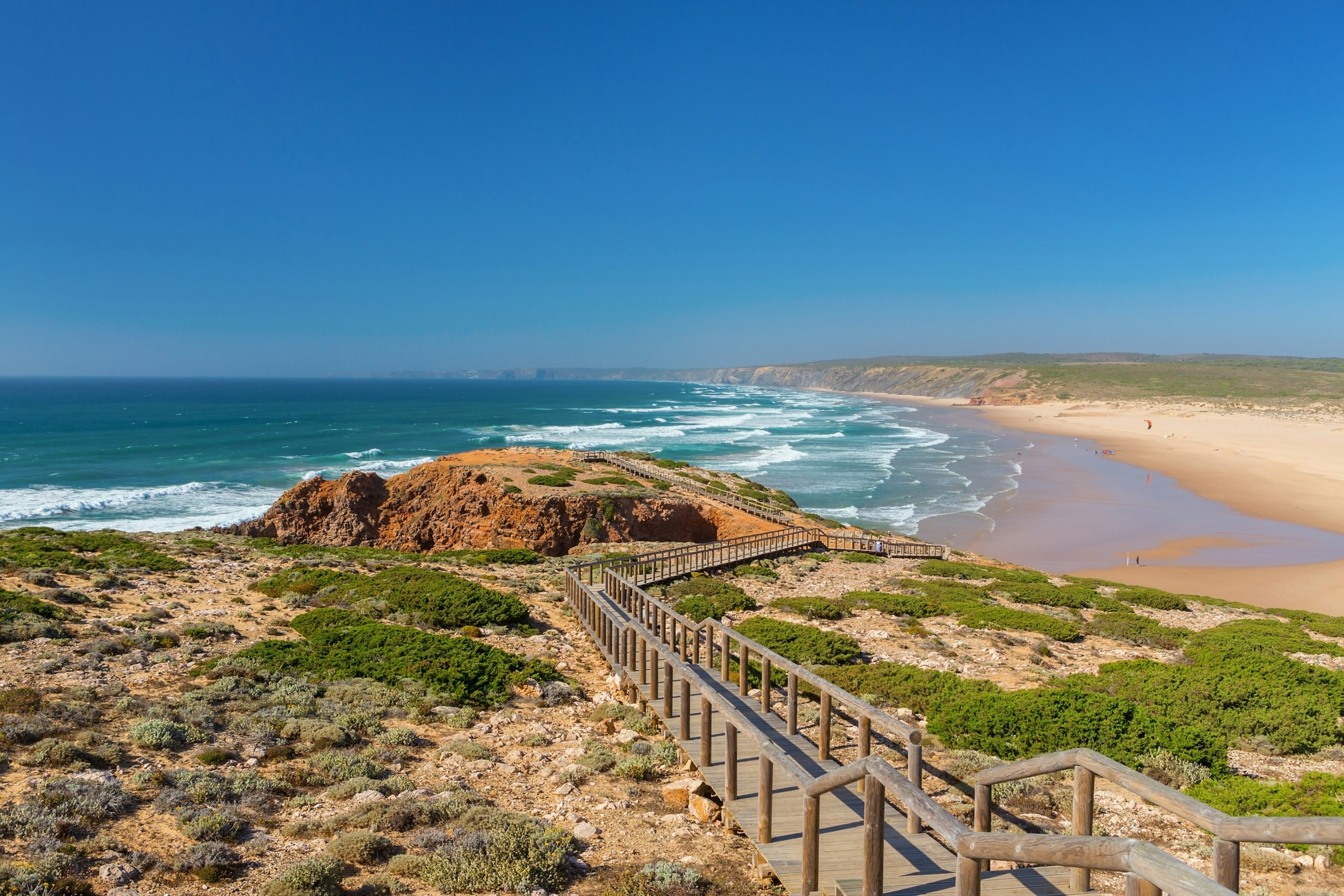 A wooden walkway traverses dunes near a beach