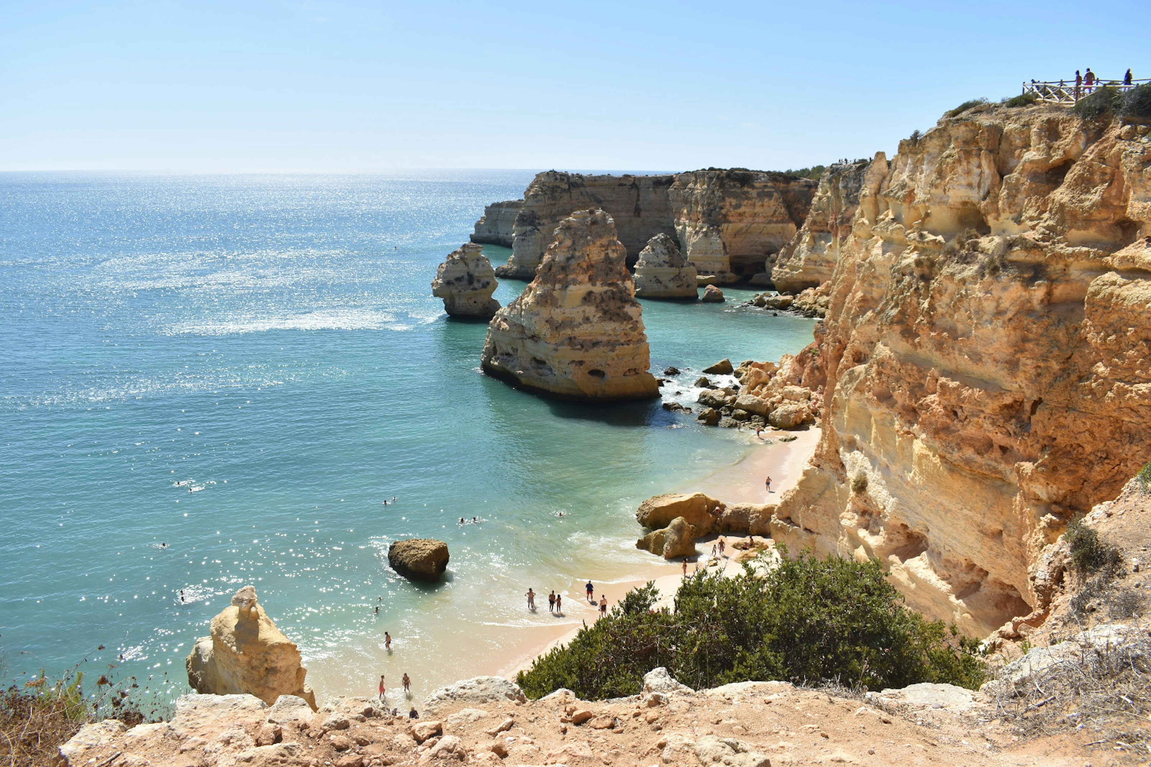 A view of the beach filled with people from high above on top of a cliff.