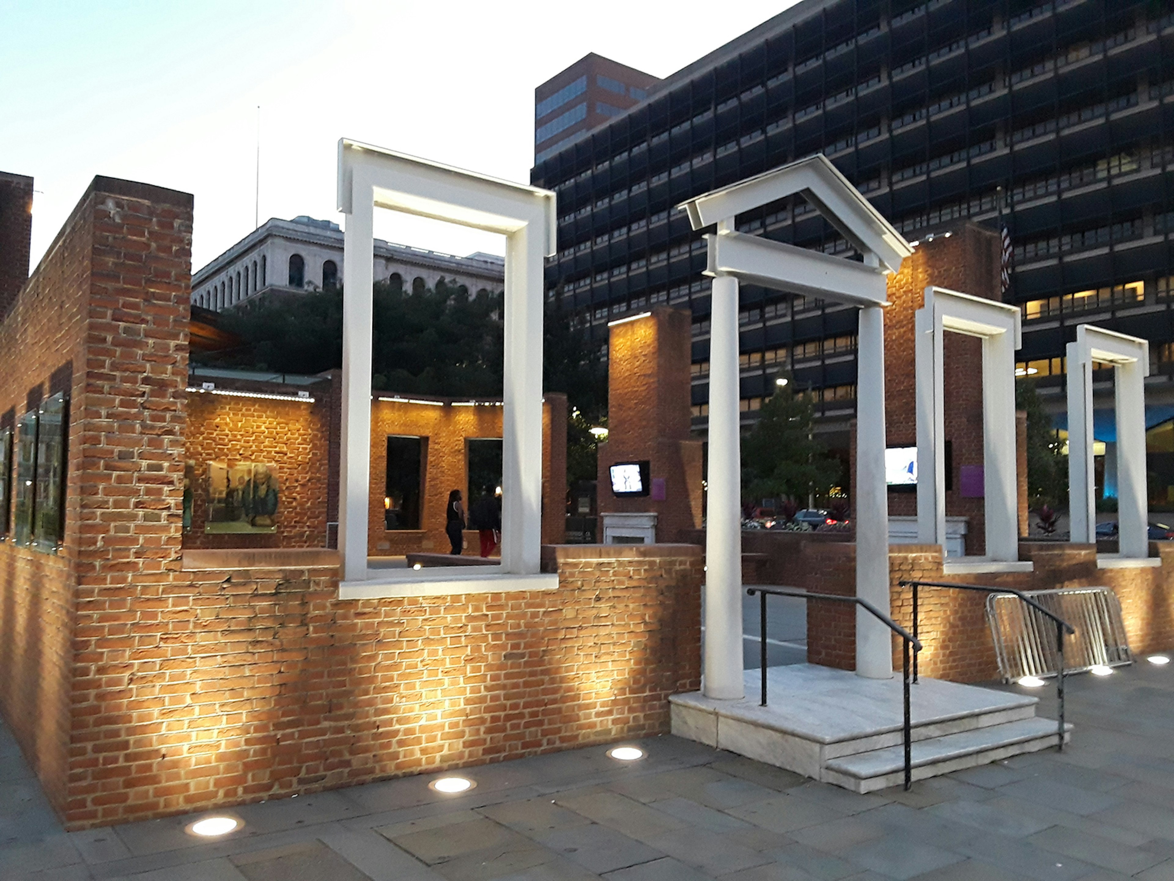 The facade of a colonial-era home where George Washington once lived, now an open-air museum, is lit up at night, with a modern building in the background