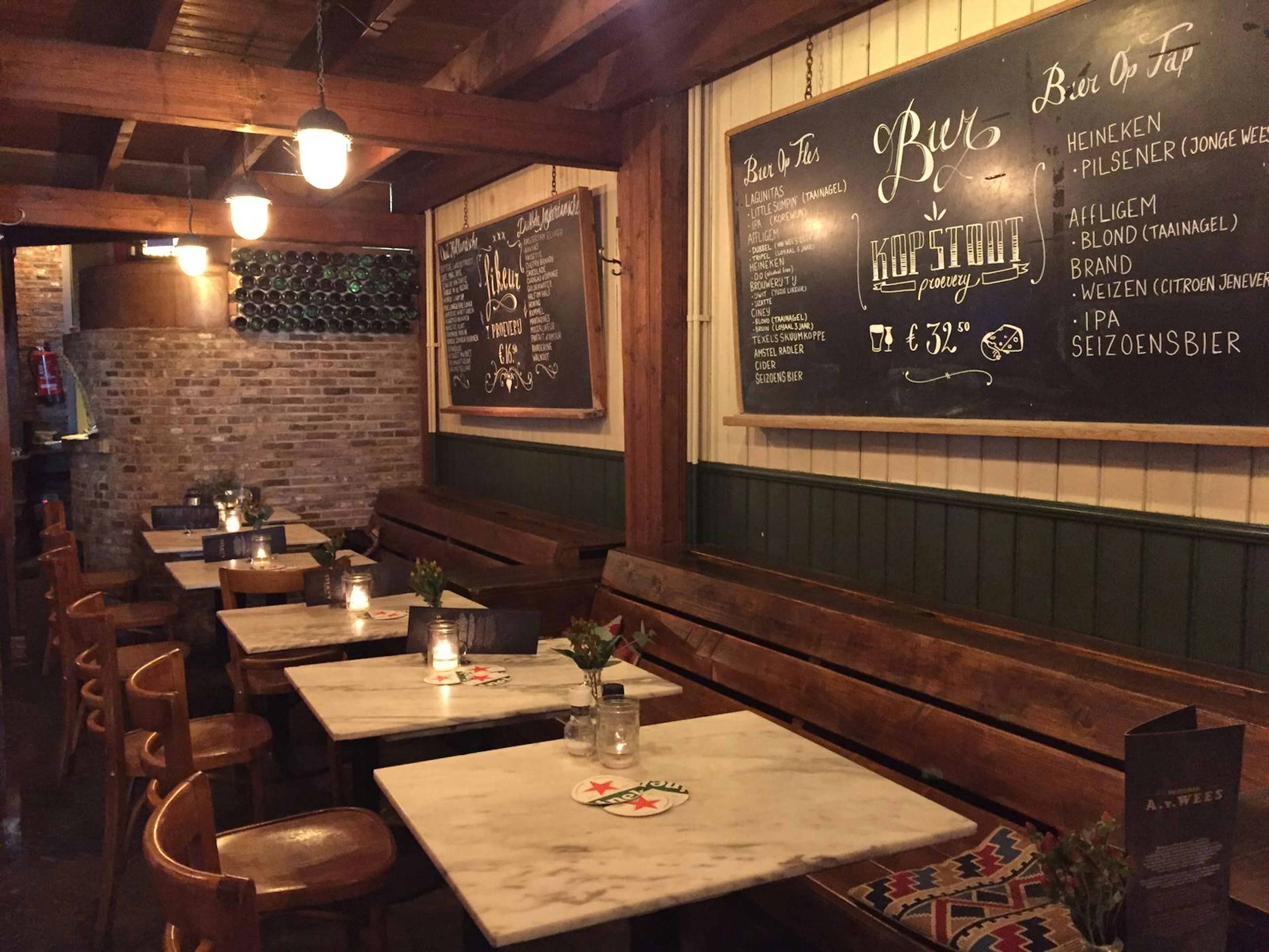 A lowly-lit, but atmospheric interior of a bar in Amsterdam; the walls are lined with wood, with a line of square marble-topped tables; they serve jenever with beer