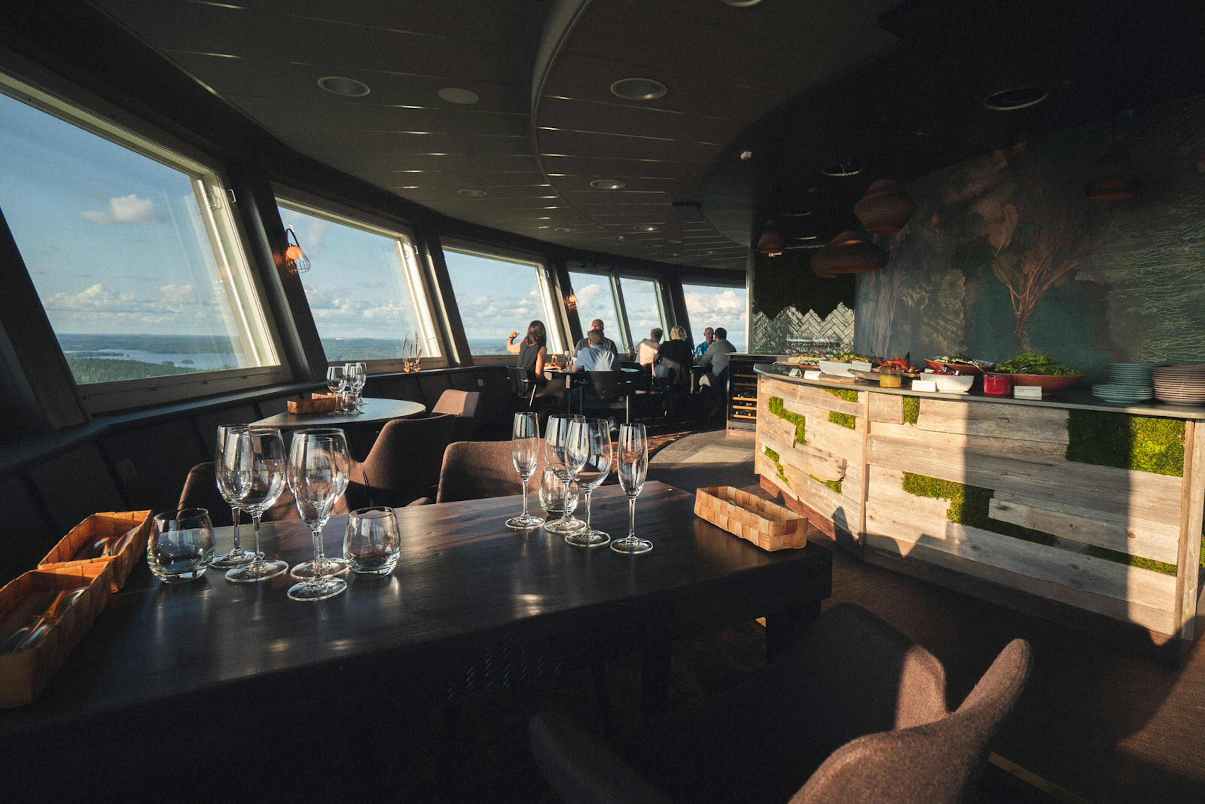 A view of the interior of Puijo Tower Restaurant in Finland. The restaurant gives panoramic views of the area and is decorated in dark, cosy colours with natural wood and moss on the walls.