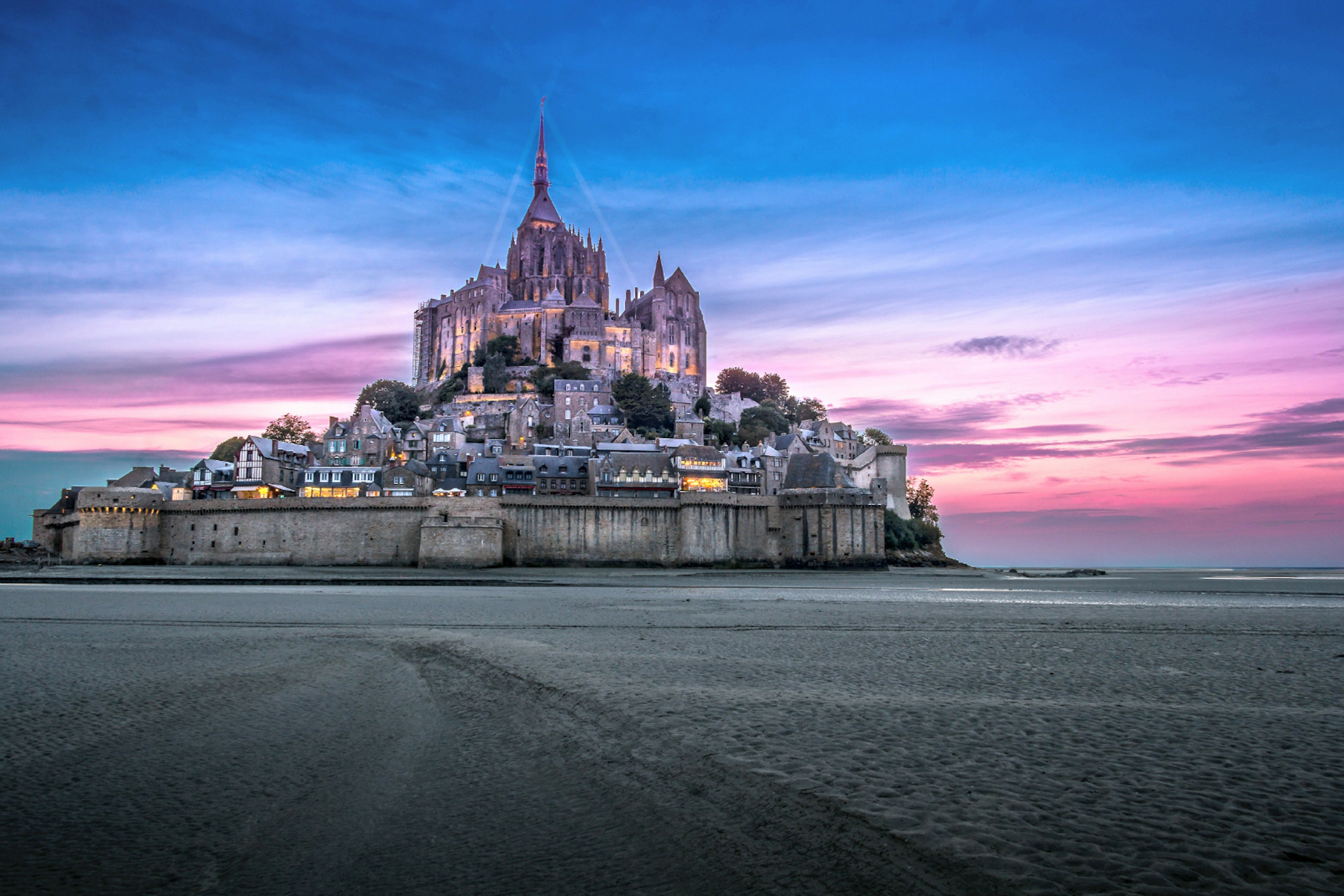 The magical abbey of Mont St-Michel against a very dramatic colourful sunset. The abbey sits across a plain of smooth white sand