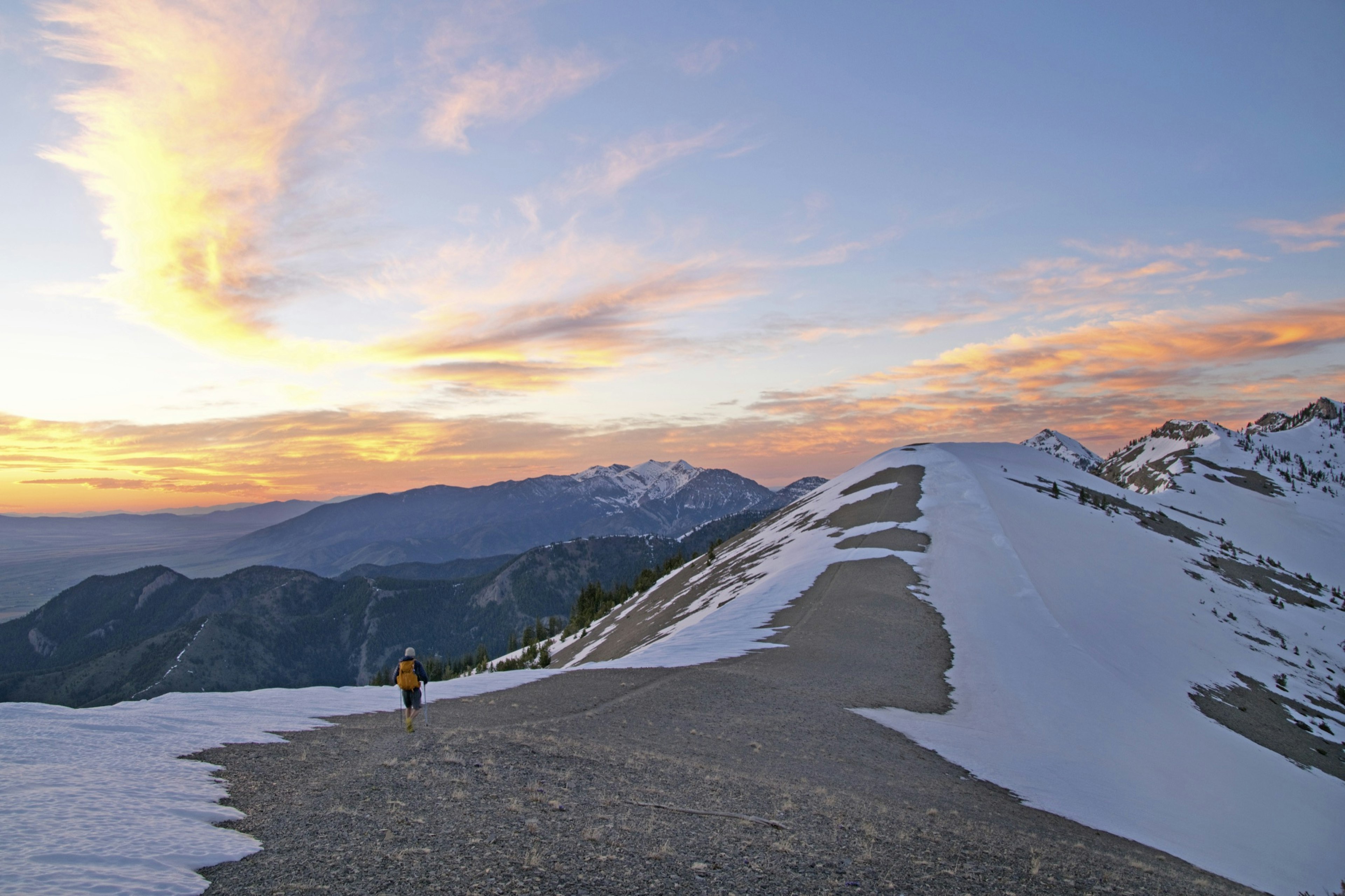 A backpacker walks along a ridge in Montana as the snow is just barely starting to recede from the trail