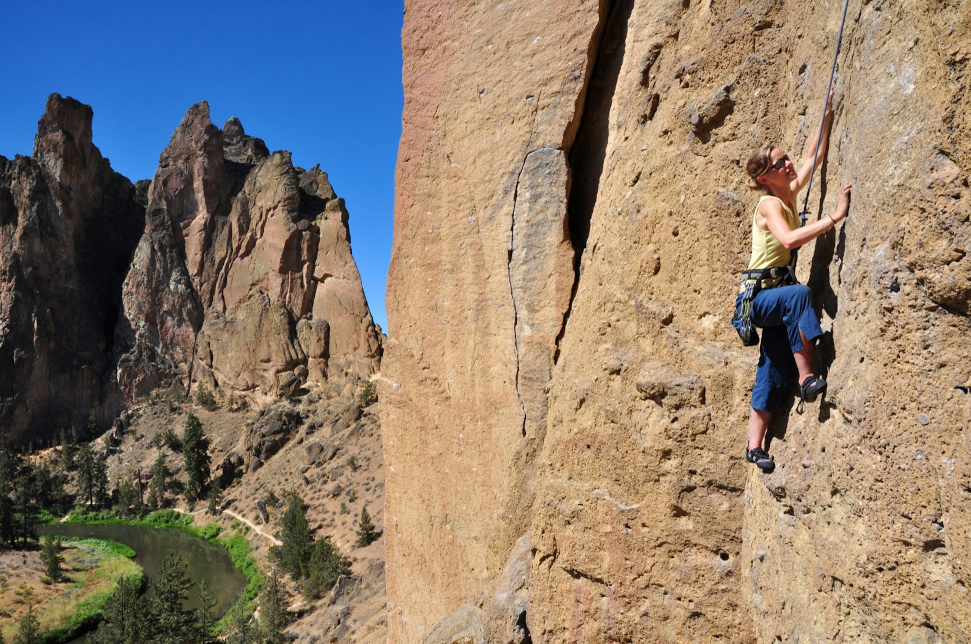 A woman climbs a sheer rock wall far above the verdant ground near Bend, Oregon