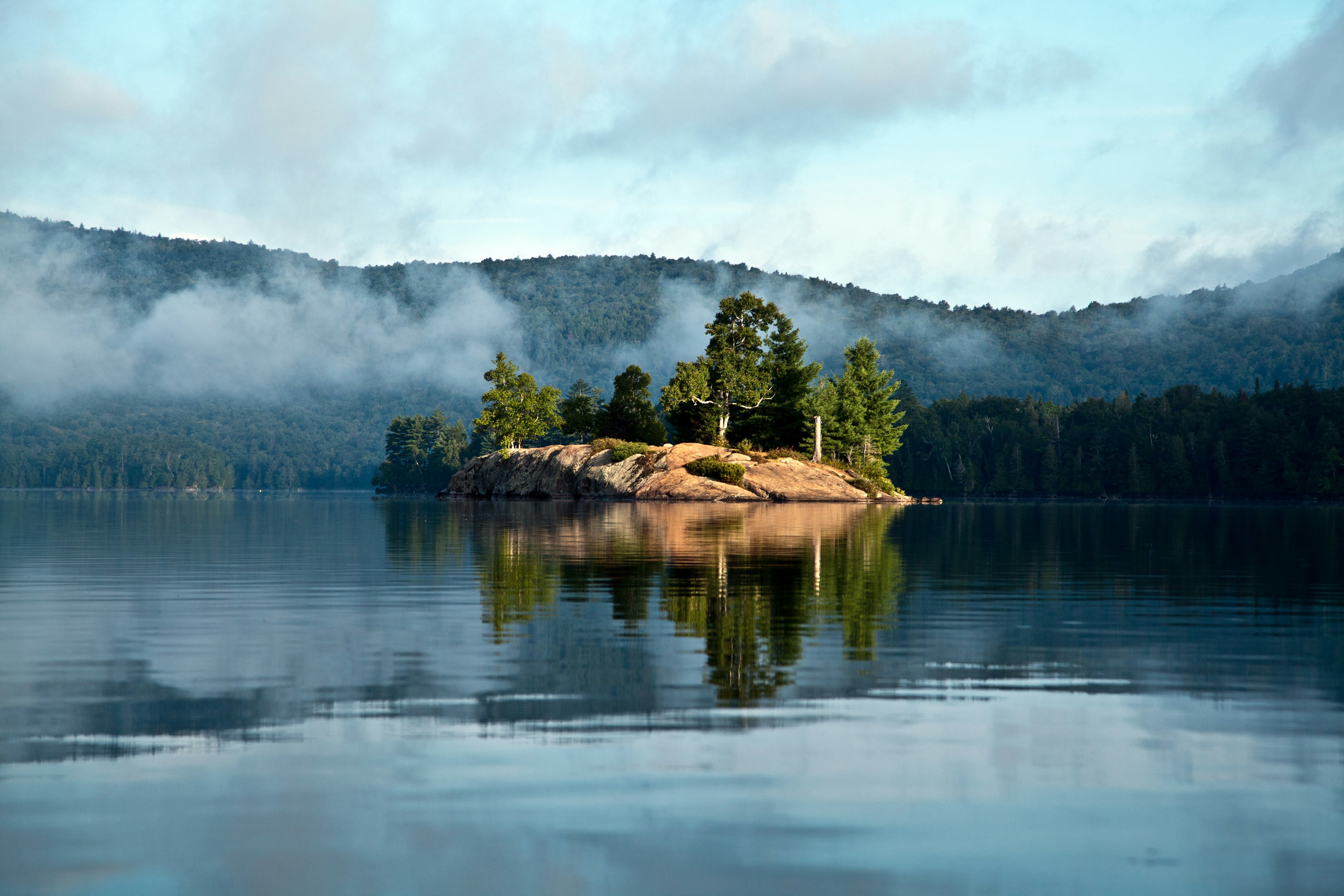 A small island sits in the middle of a blue lake, surrounded by misty hillsides