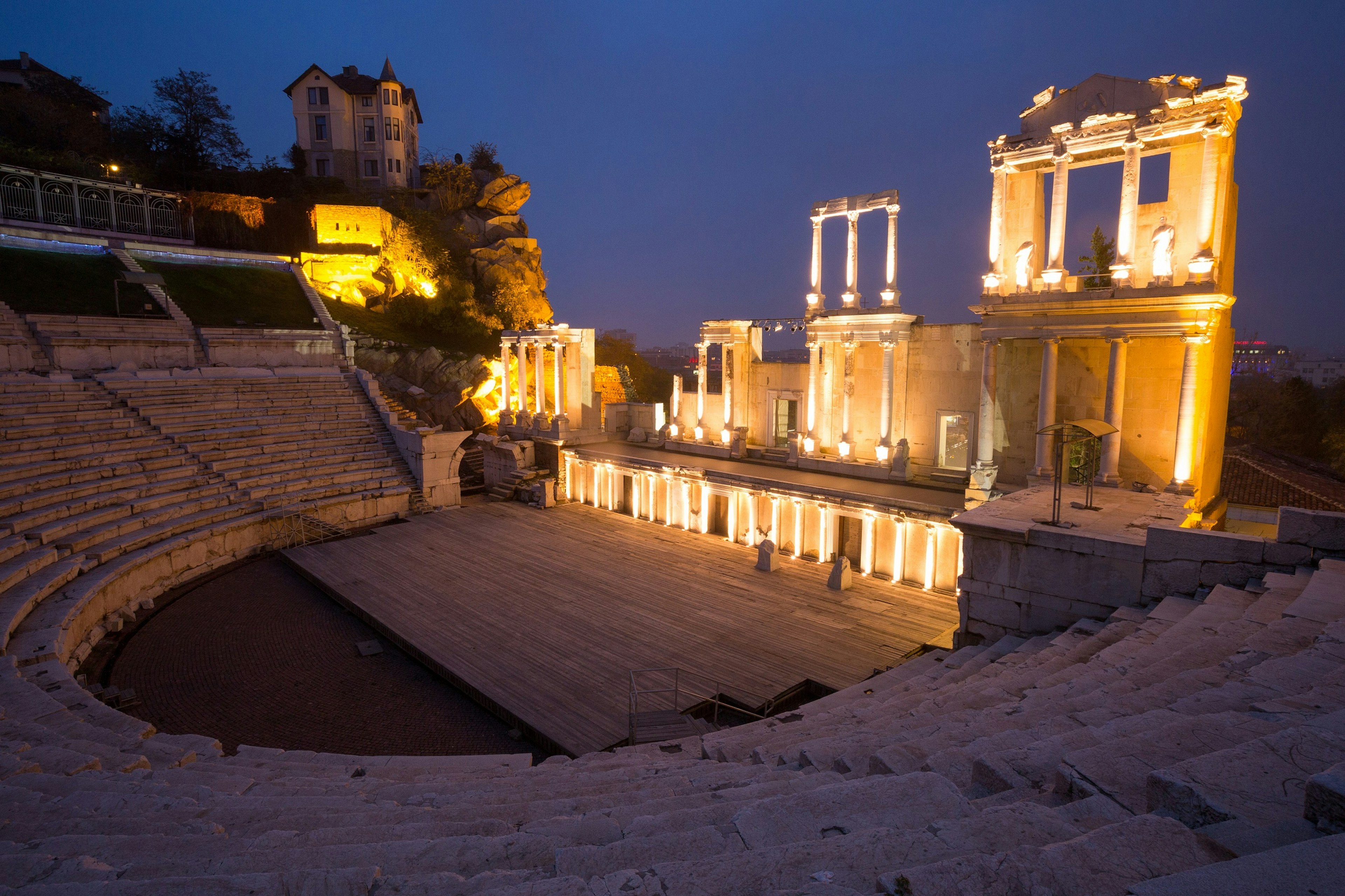 Some ruined columns and an ancient tiered stone seating area of an amphitheatre lit up at night