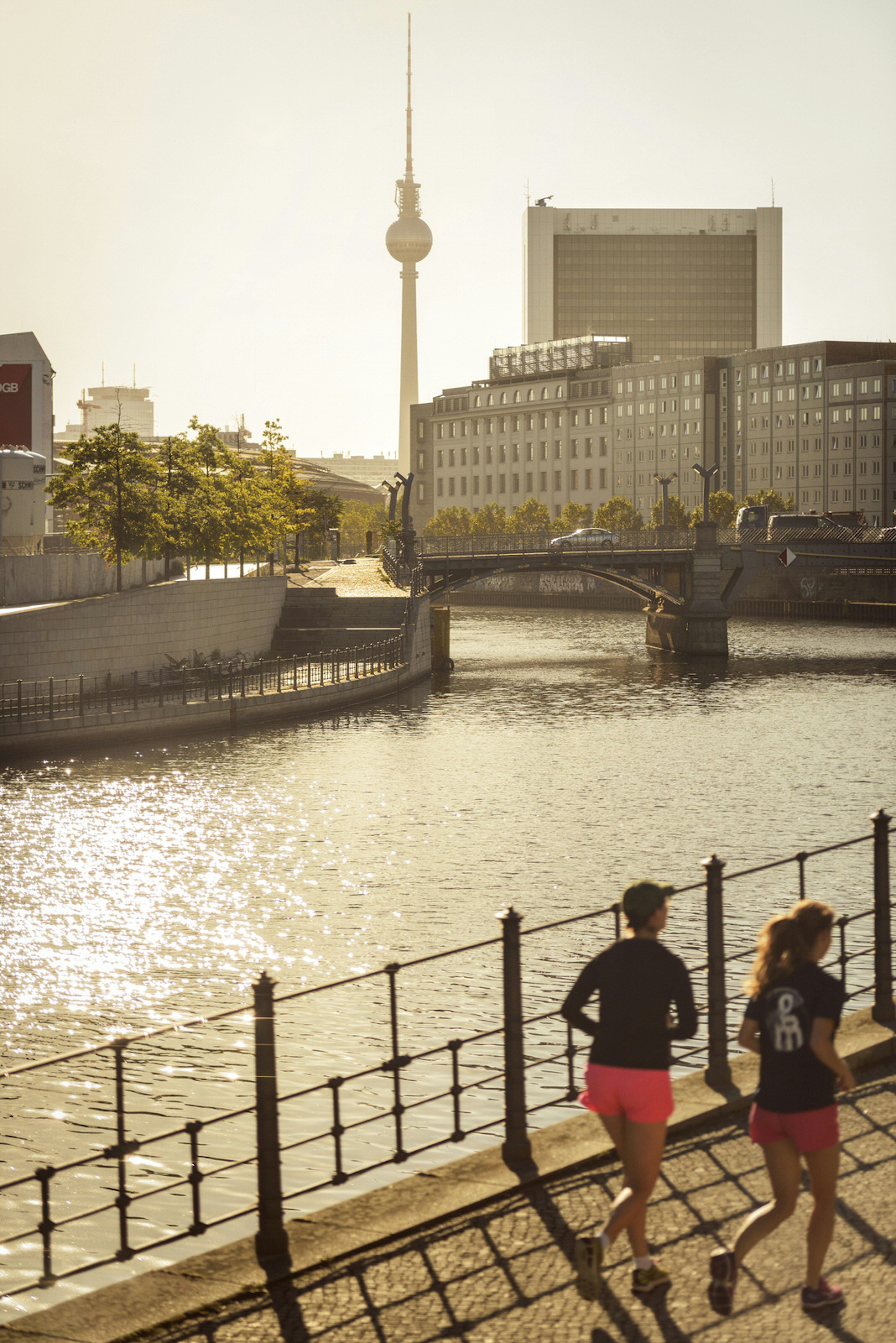 Two people are running at sunset along the paved bank of the hemmed in Spree River in Berlin