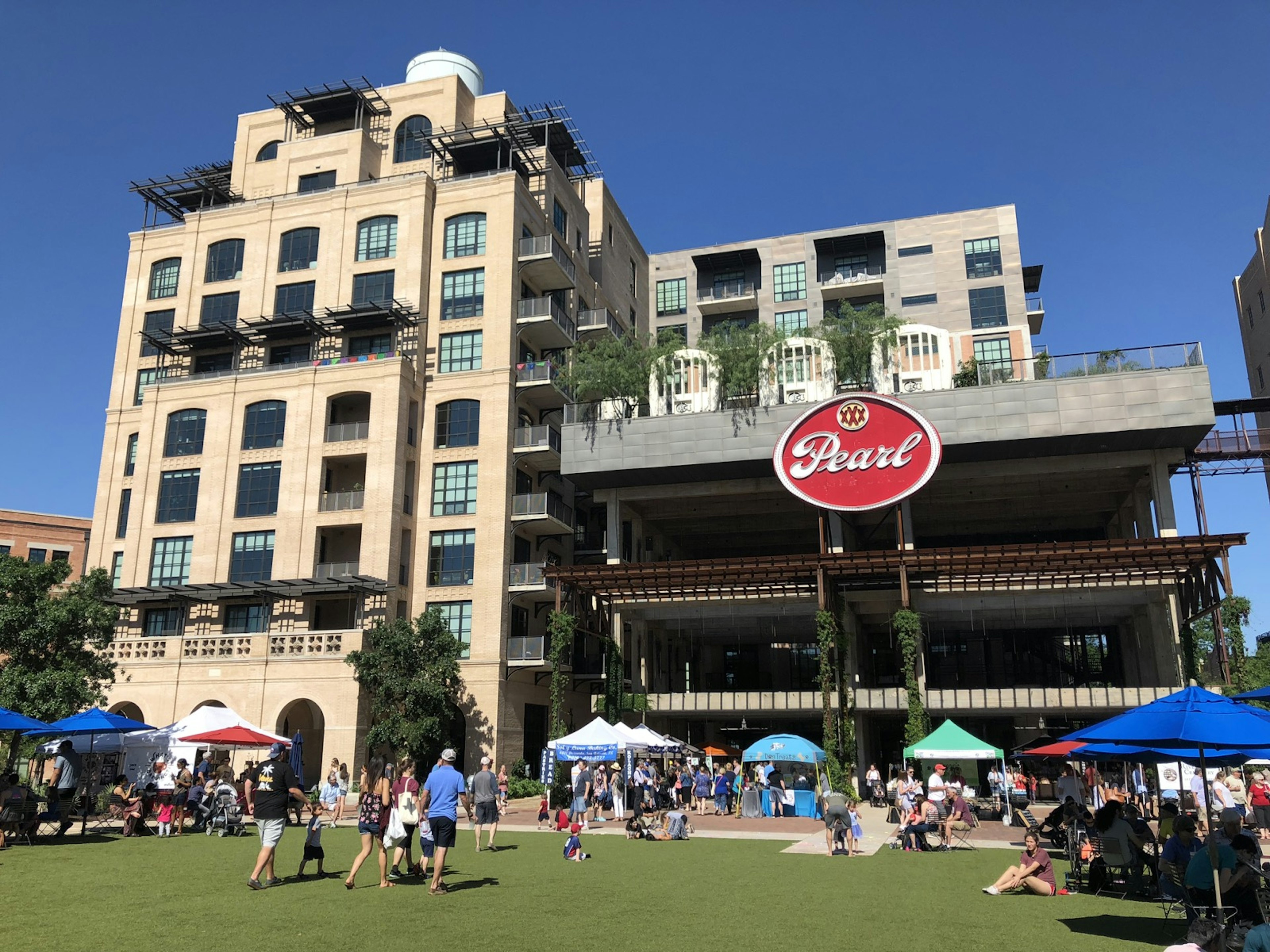 A broad green space with lots of meandering people is seen in front of an old building with a red oval sign that reads 'Pearl' © Vicki Arkoff / Lonely Planet