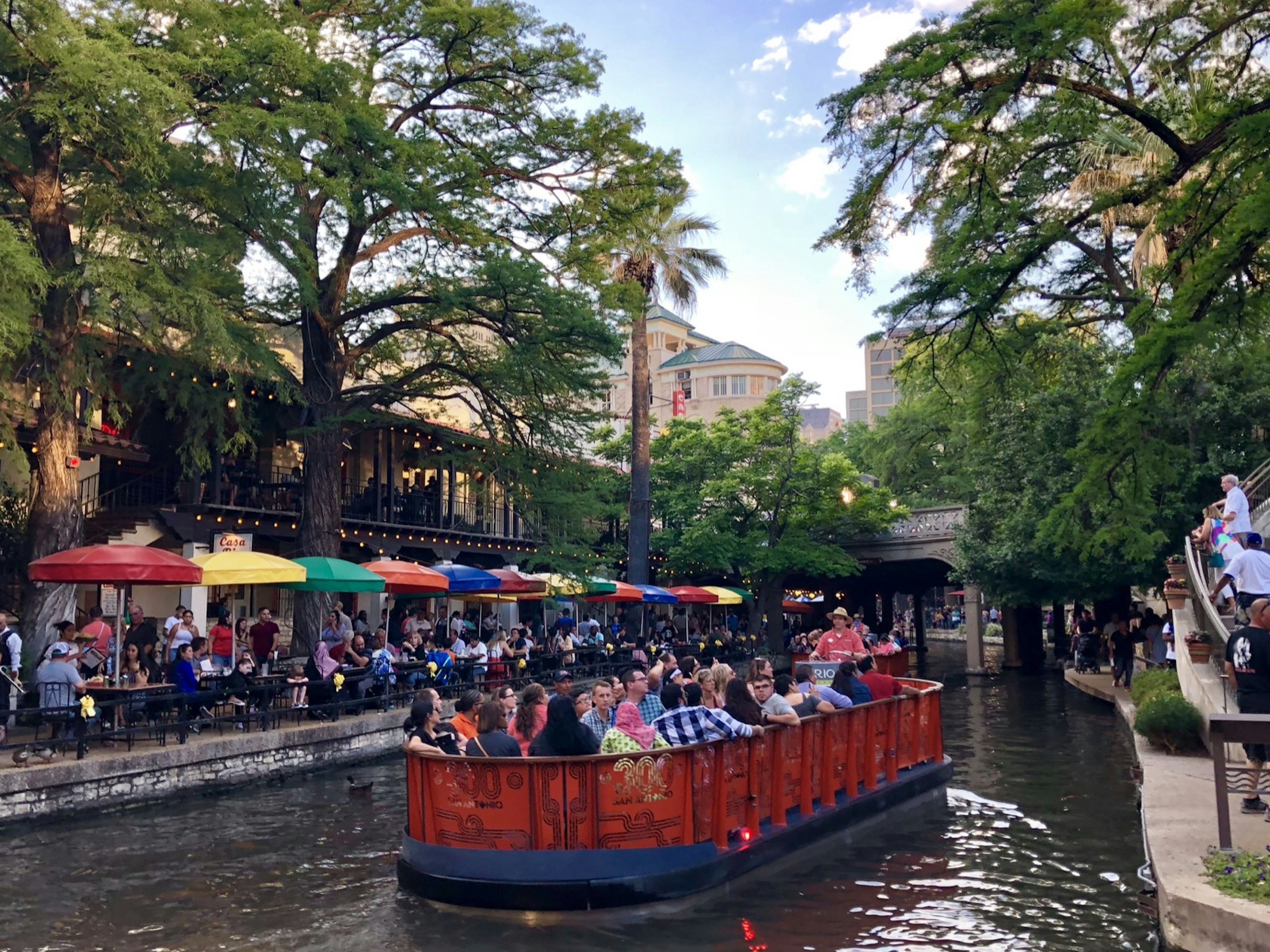 A river barge with diners floats down the canal in San Antonio with other diners under colorful umbrellas on the bank of the canal © Vicki Arkoff / Lonely Planet