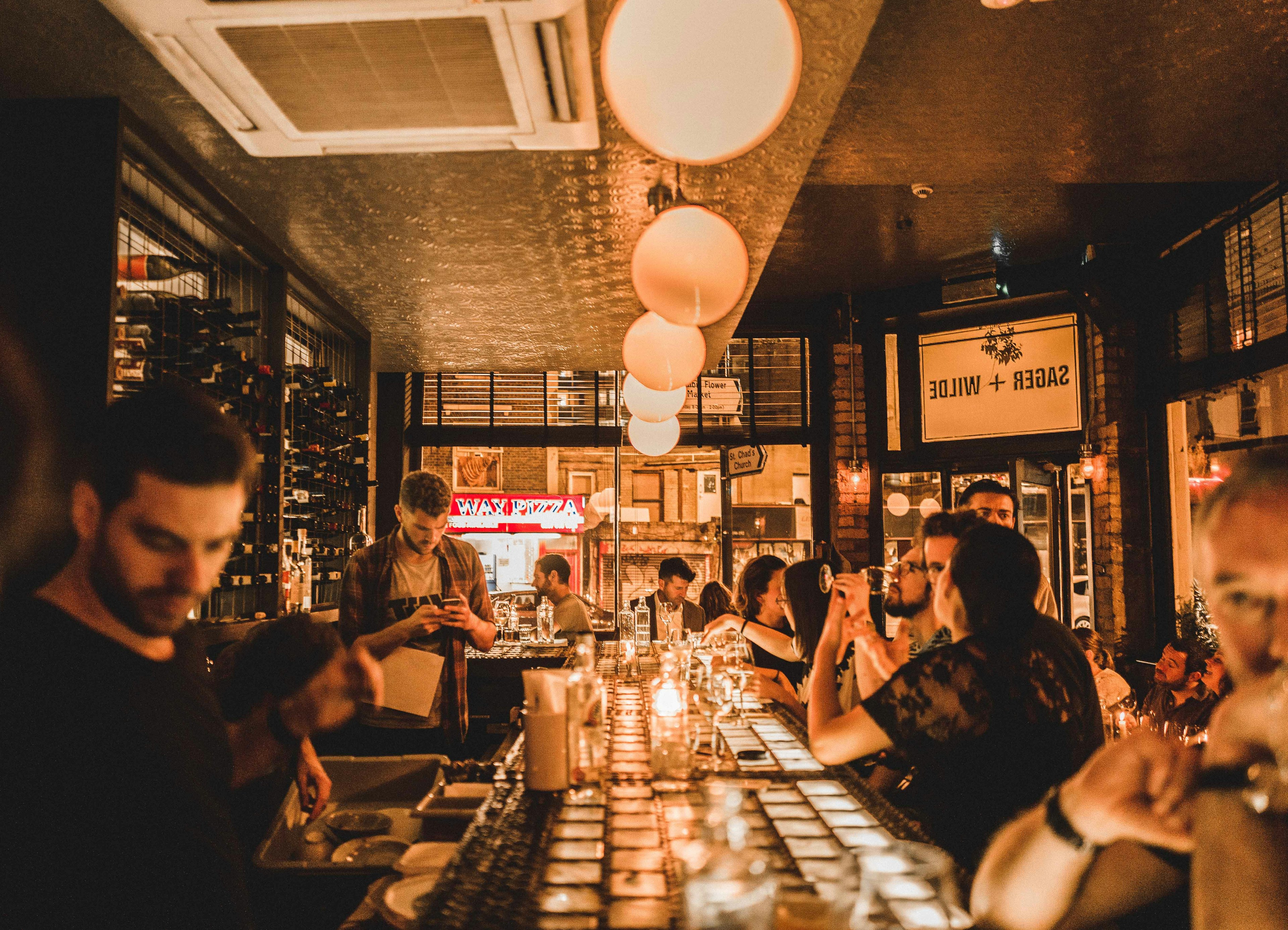 People seated around the bar of Sager + Wilde in east London at night, basked in an amber glow.