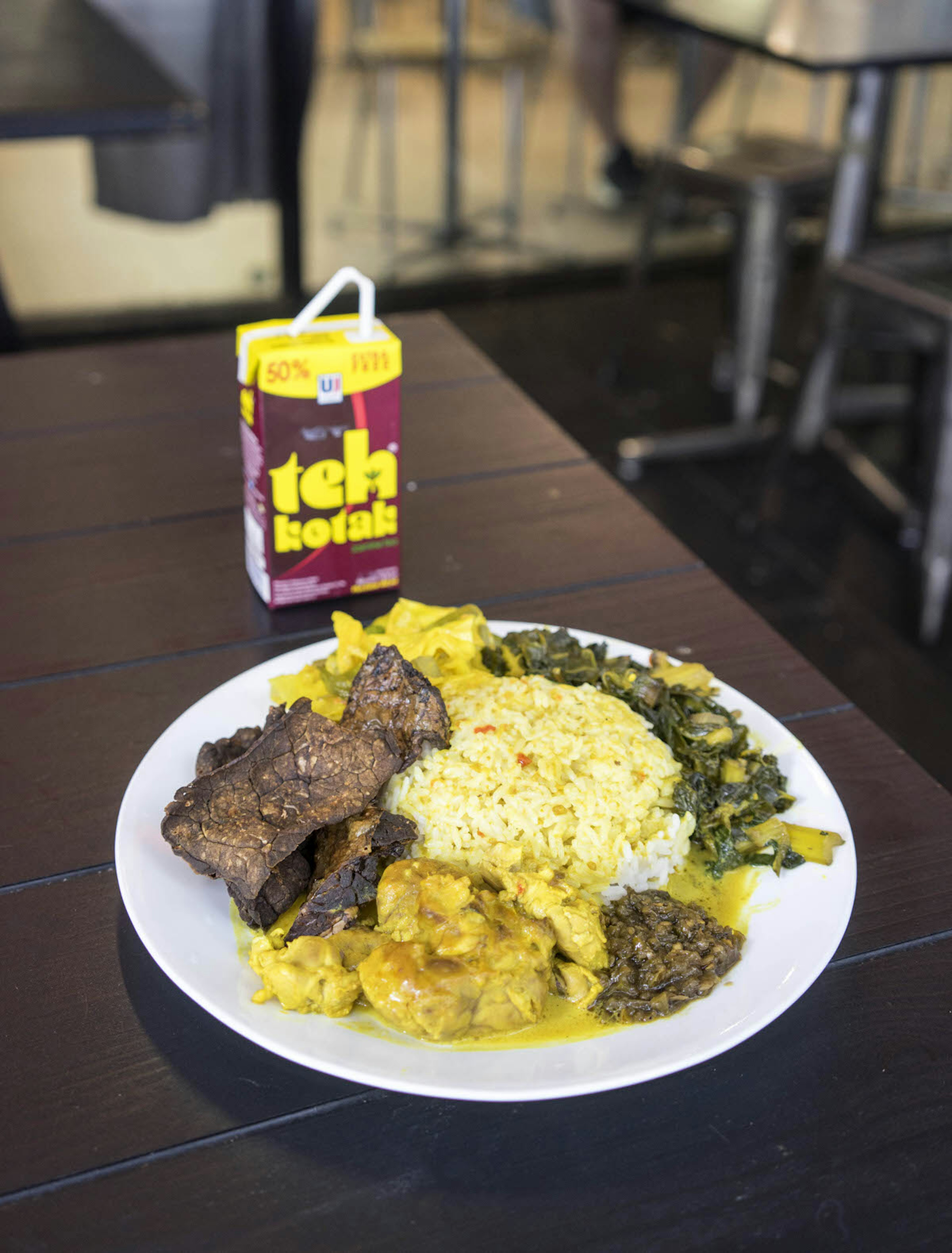 Salero Kito, Padang food, in Melbourne. The dish is served on a dark wooden table alongside a carton of juice. There is rice, brown meat, sauce and green vegetables on the plate.