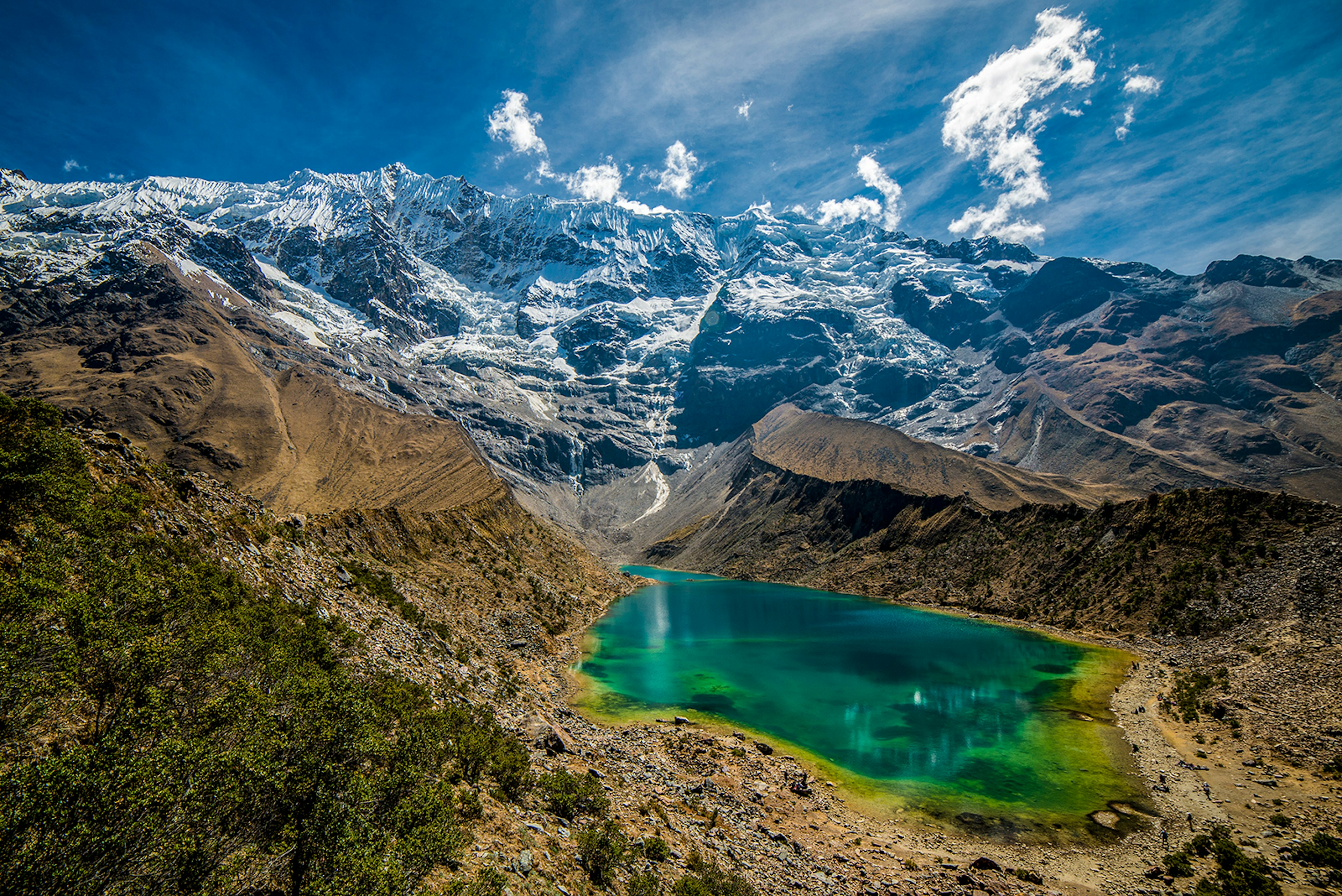 A blue glacial lagoon sits against a backdrop of craggy, snowy mountains