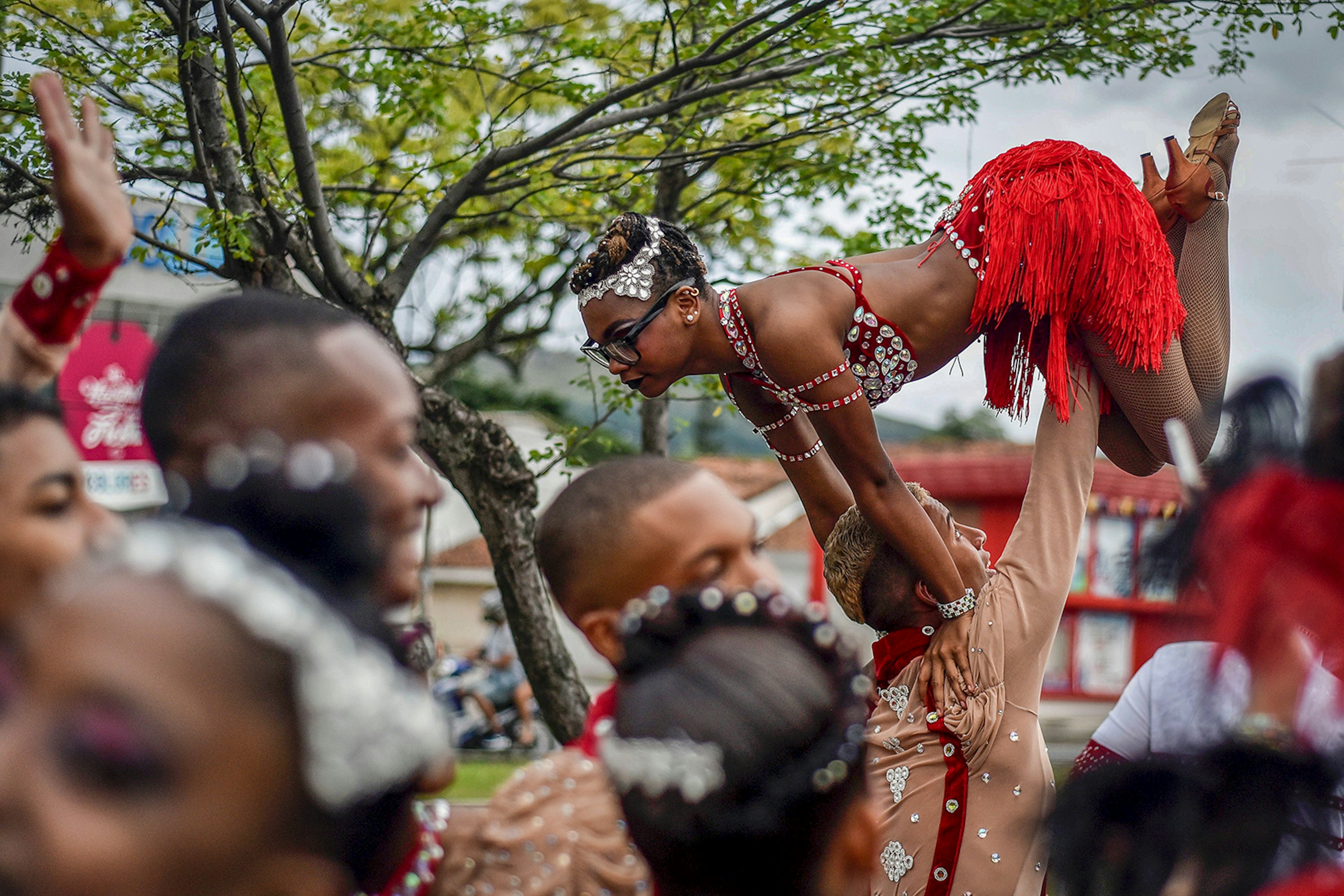 A man holds a woman dressed in red fringe and rhinestones above his head in a salsa dance lift