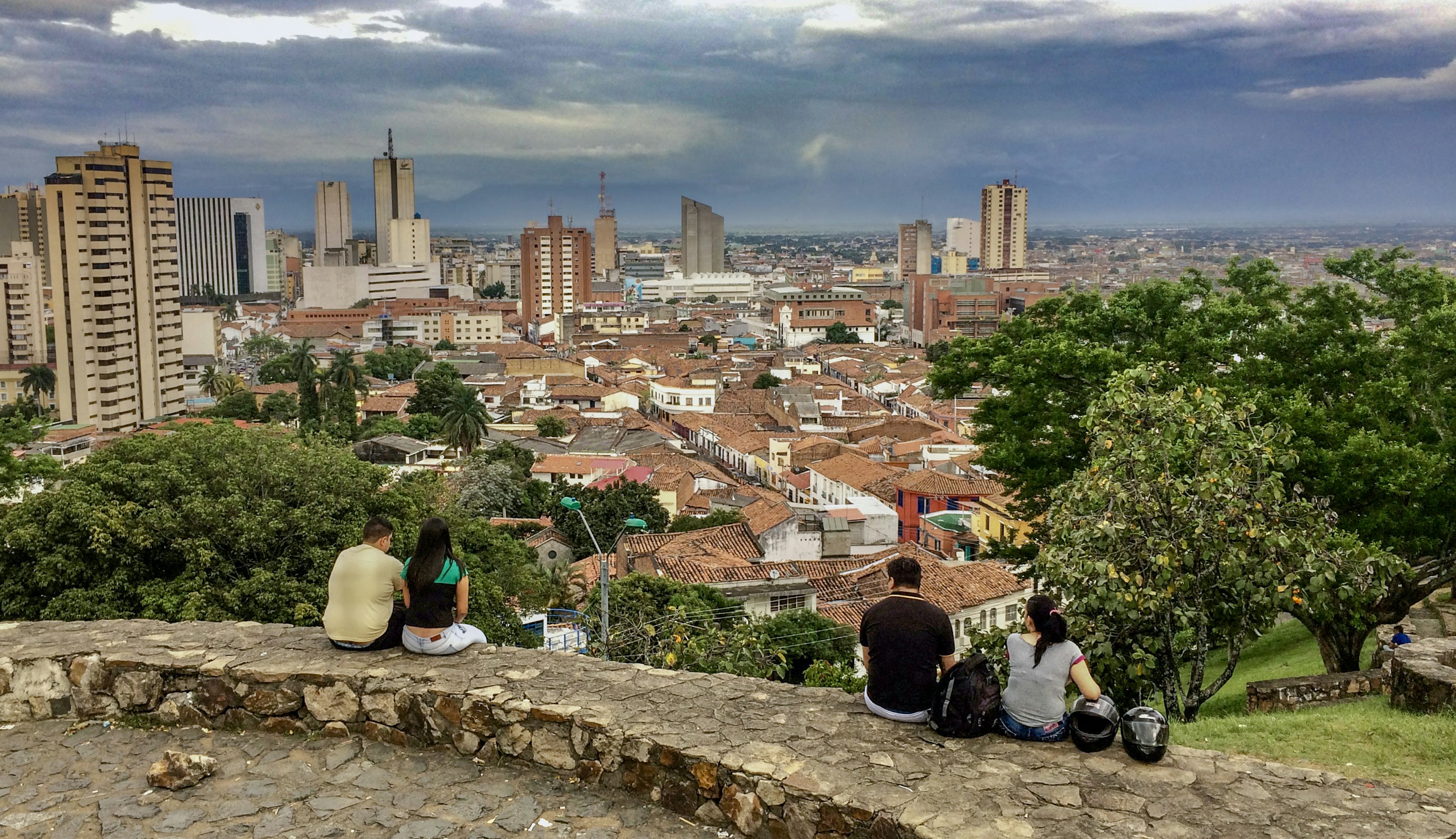 Four people sit on a rock wall overlooking the city of Cali