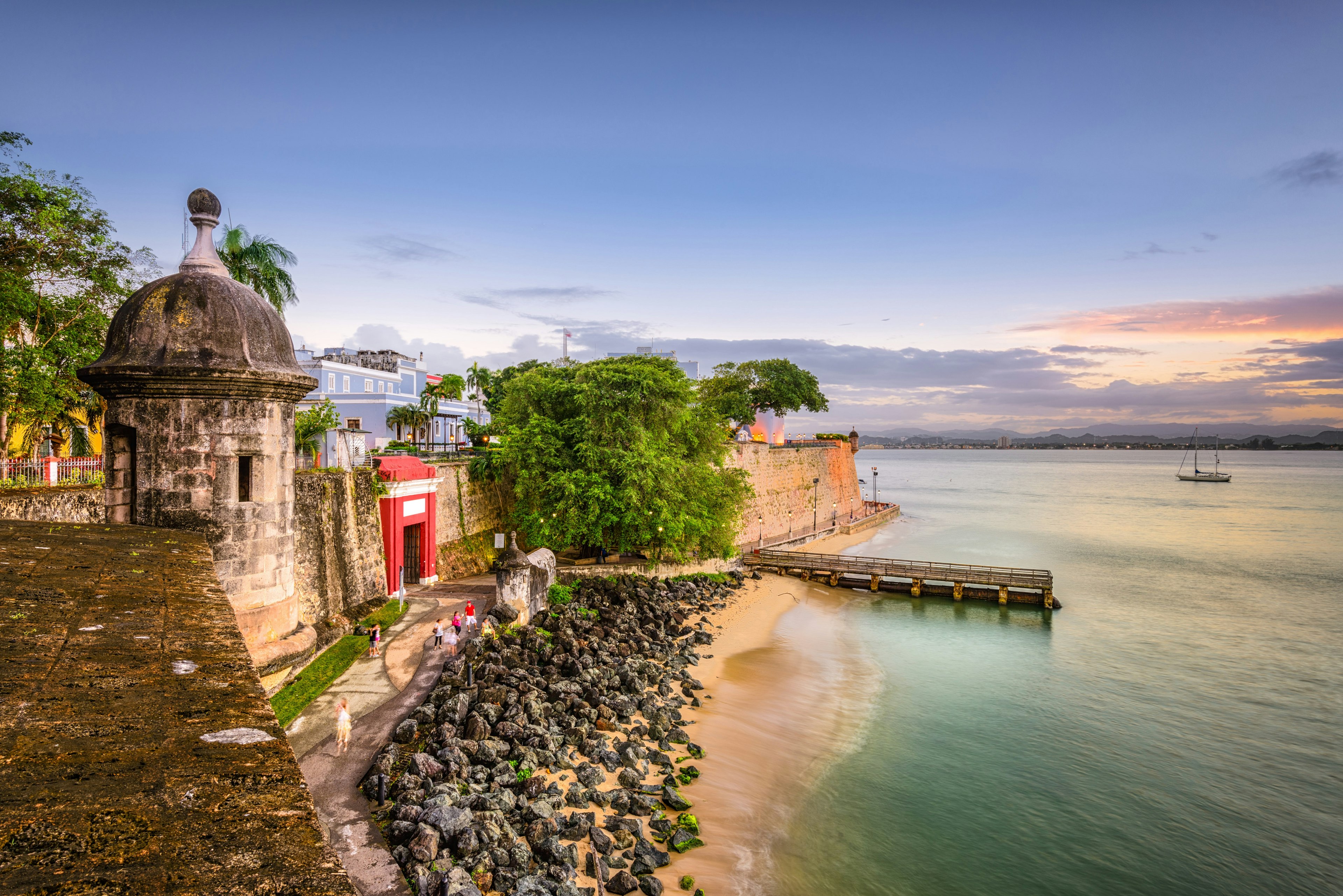 A view of the coast of San Juan, with the old stone city walls visible behind a small stretch of white sand and a blue ocean.