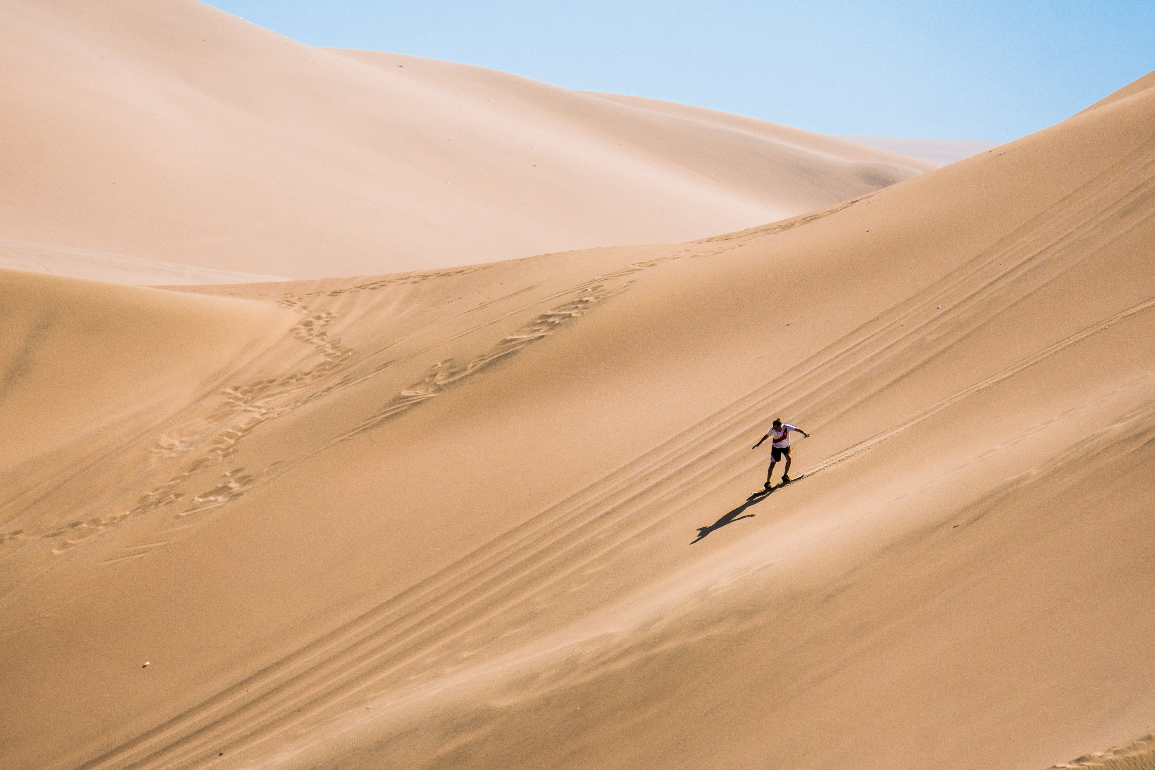 Wide shot of a man sandboarding down a large dune in Peru