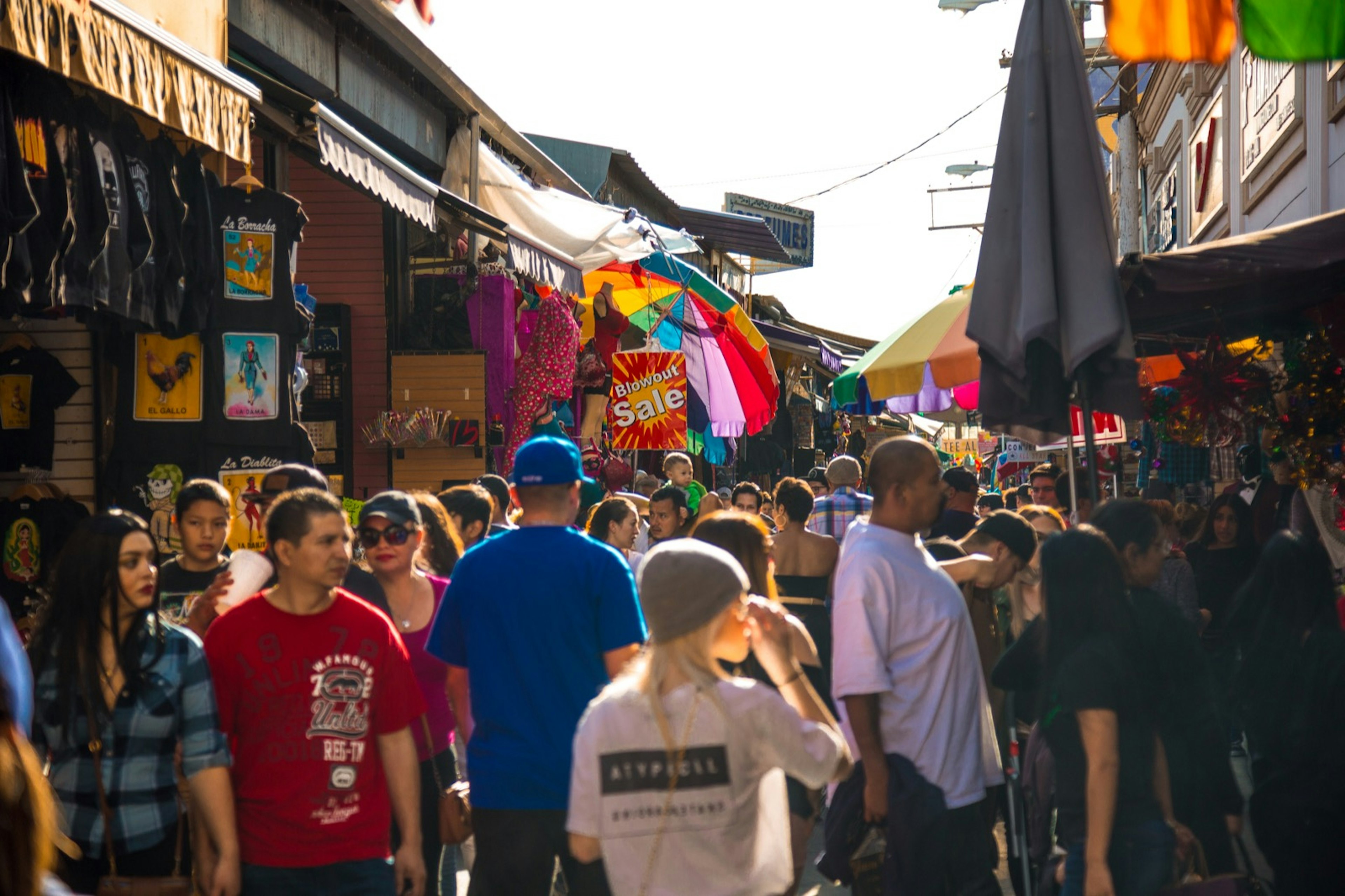 A crowd of people meanders down a narrow alley lined with shops