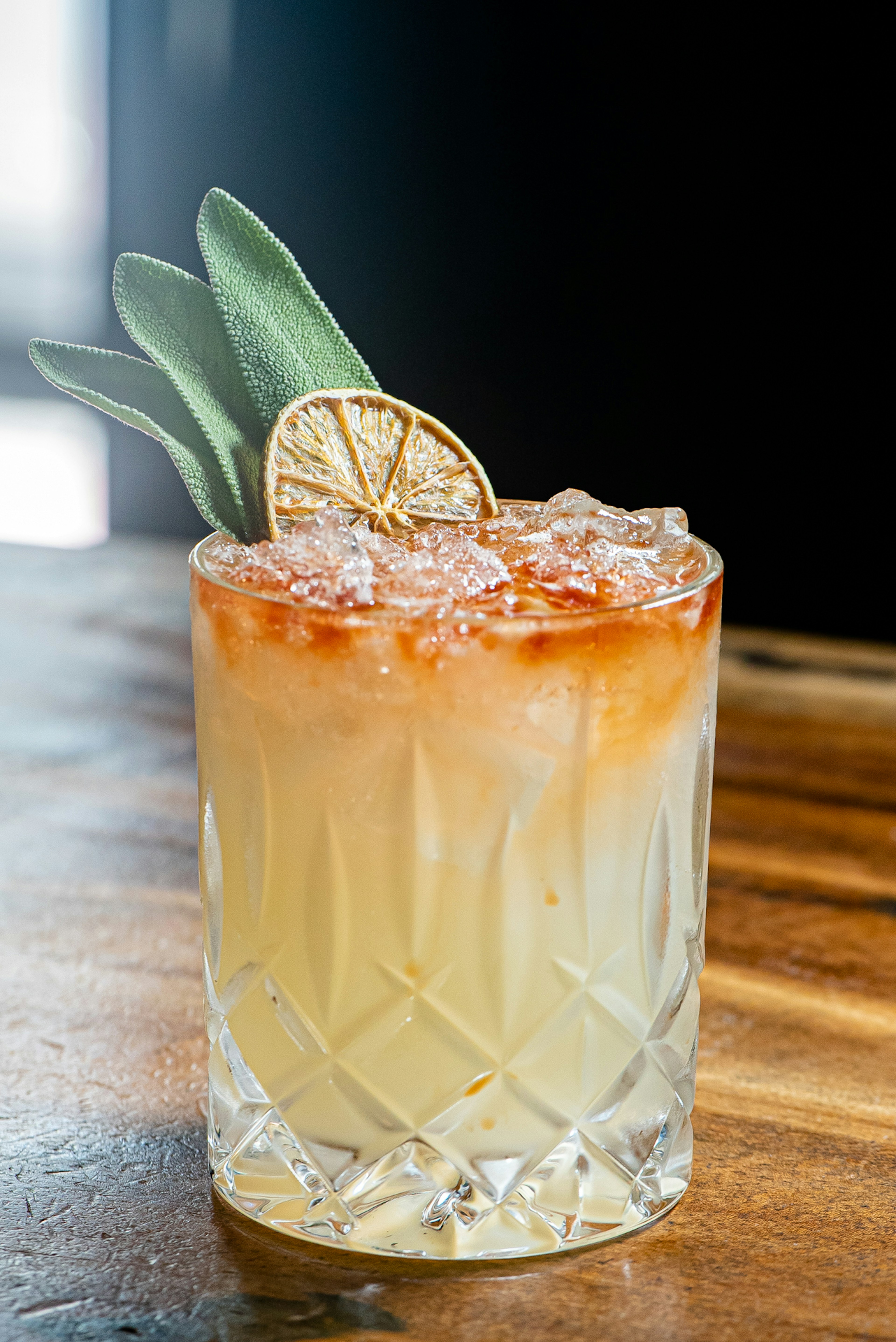 Photo of a milky cocktail in a crystal glass with ice. Decorating the glass is a slice of a dried citrus fruit and three leaves of mint.