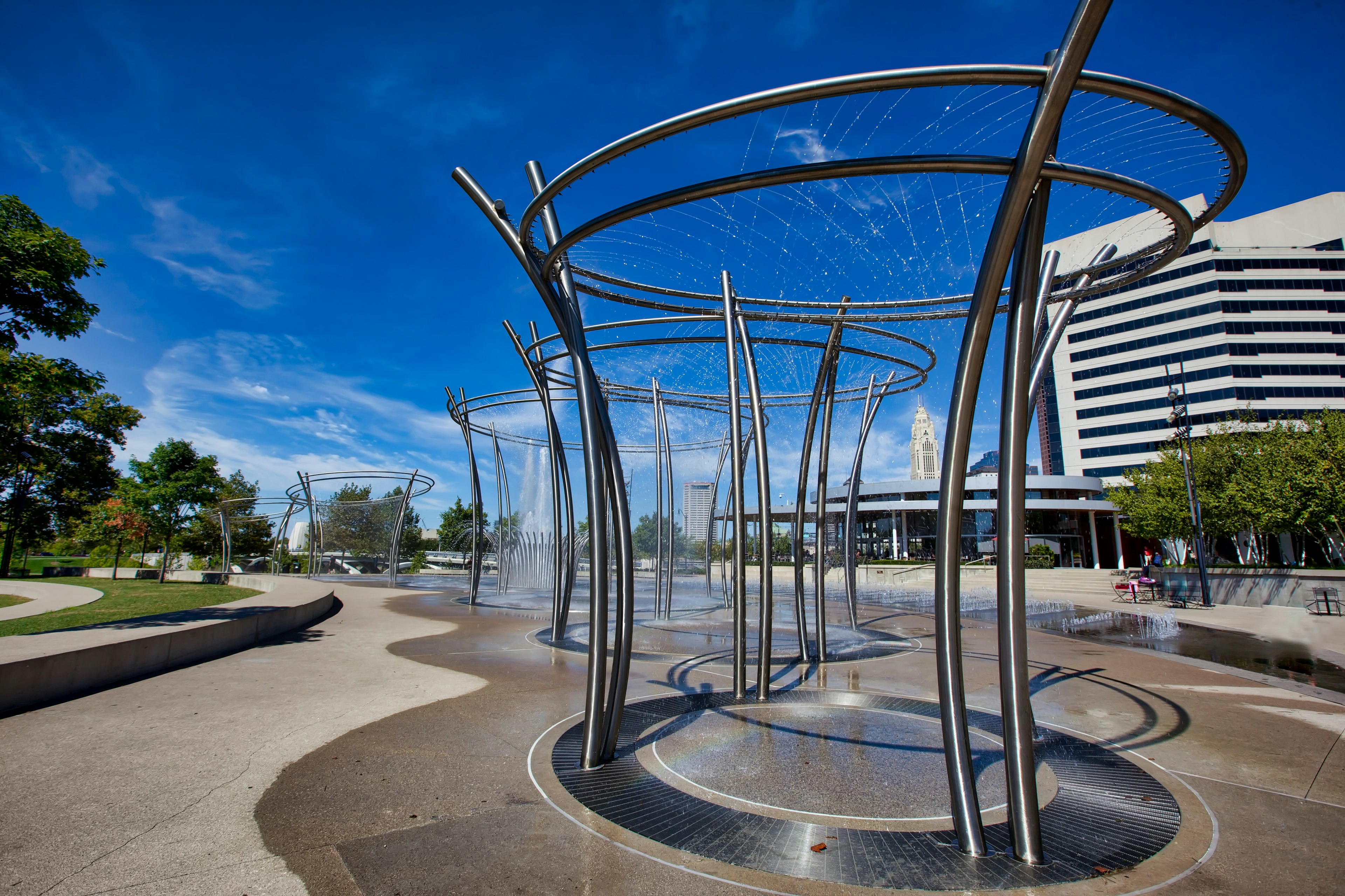 A line of metal elaborately designed fountains shoot off water in a city park along the Scioto Mile in downtown Columbus