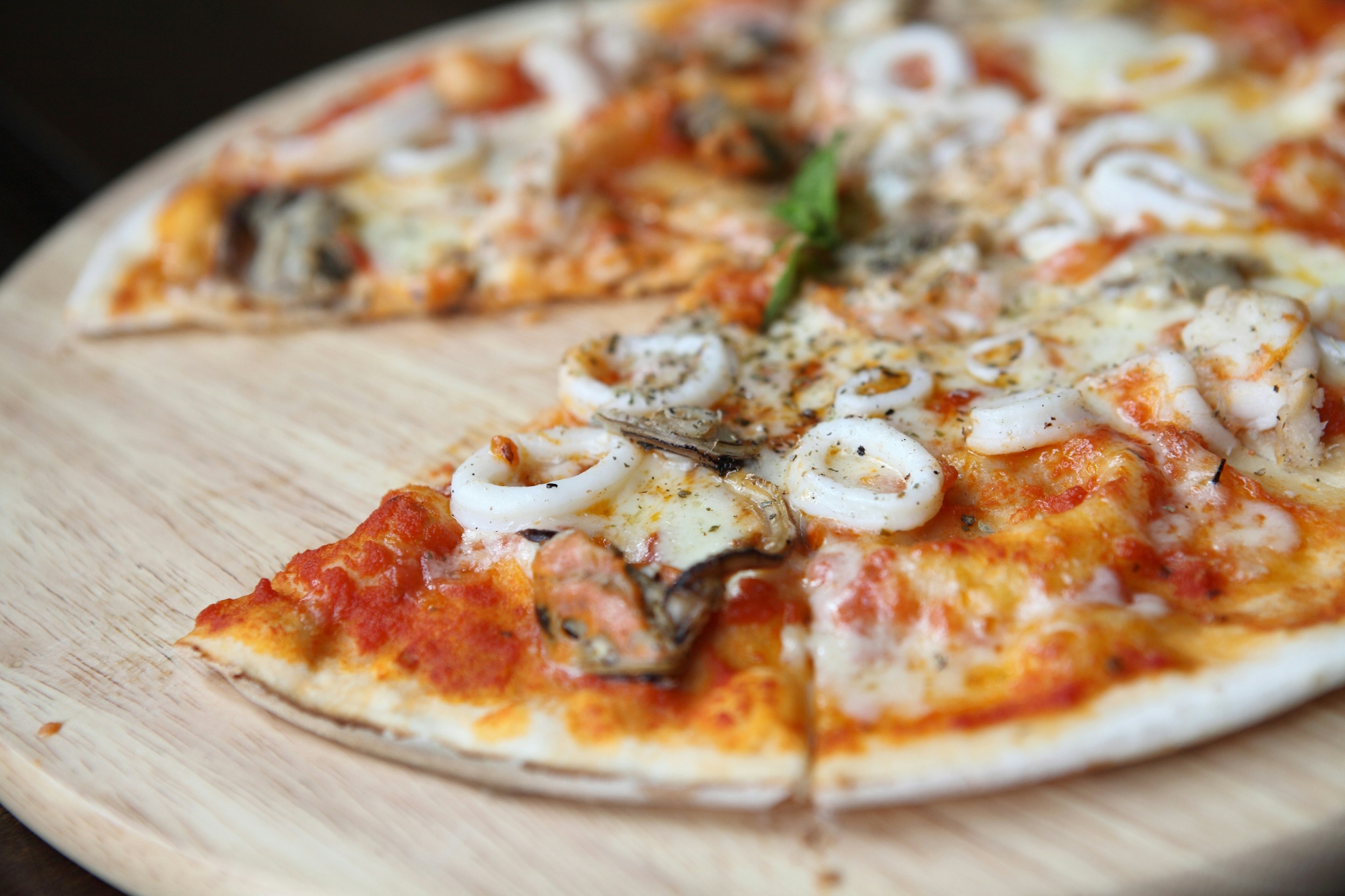 A large seafood pizza displayed on a wooden board. The tomato and cheese pizza is topped with squid, muscles and other shellfish.