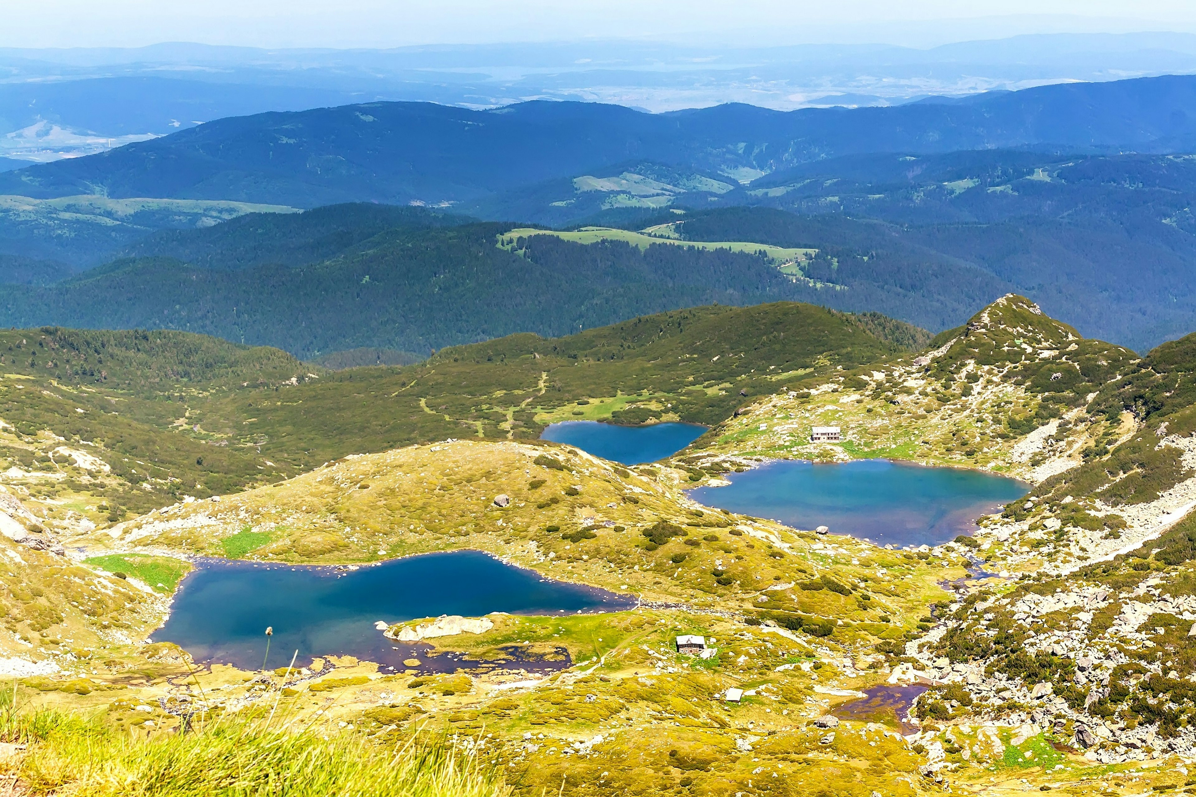 A view across a valley in a mountain range. There are three distinct lakes surrounded by grassland; and more hills in the background.