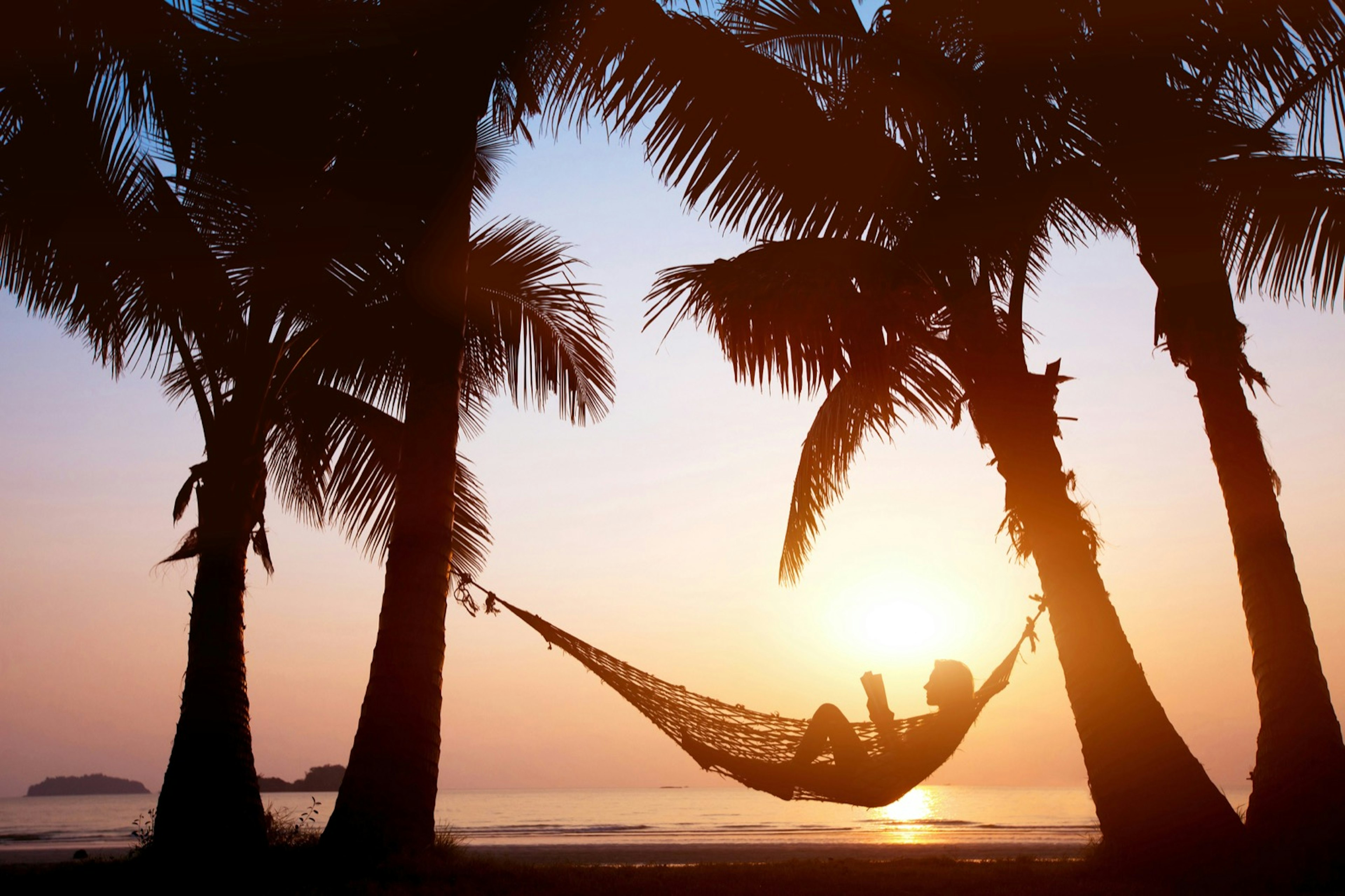 Woman reads in a hammock on a beach in the Seychelles Islands