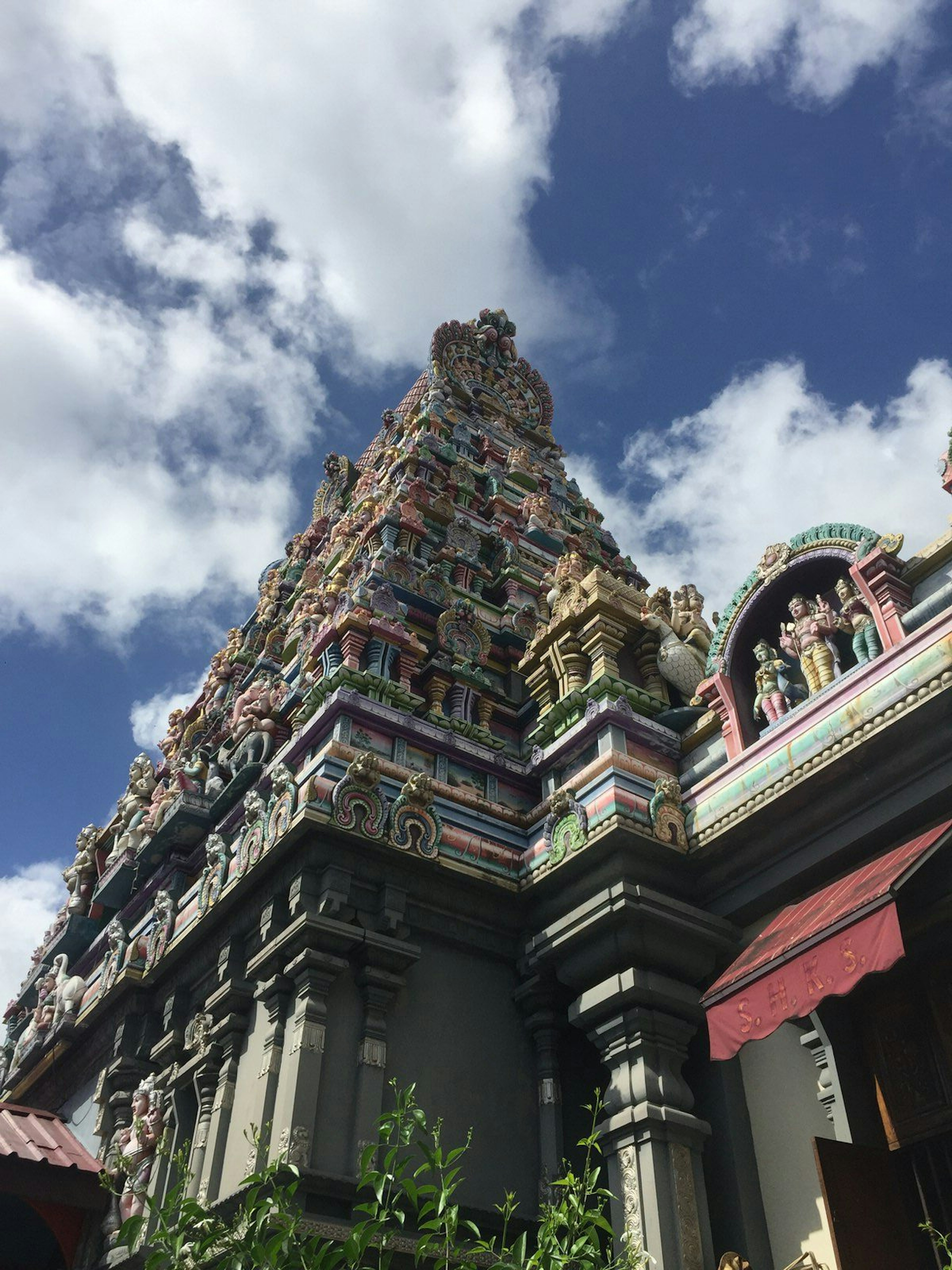 Under a blue sky dotted with white, cotton ball-looking clouds, is the tapering tower of the Hindu Sri Navasakthi Vinyagar Temple. The four-sided pyramid is adorned with numerous layers of colourful engravings © Matt Phillips / ϰϲʿ¼