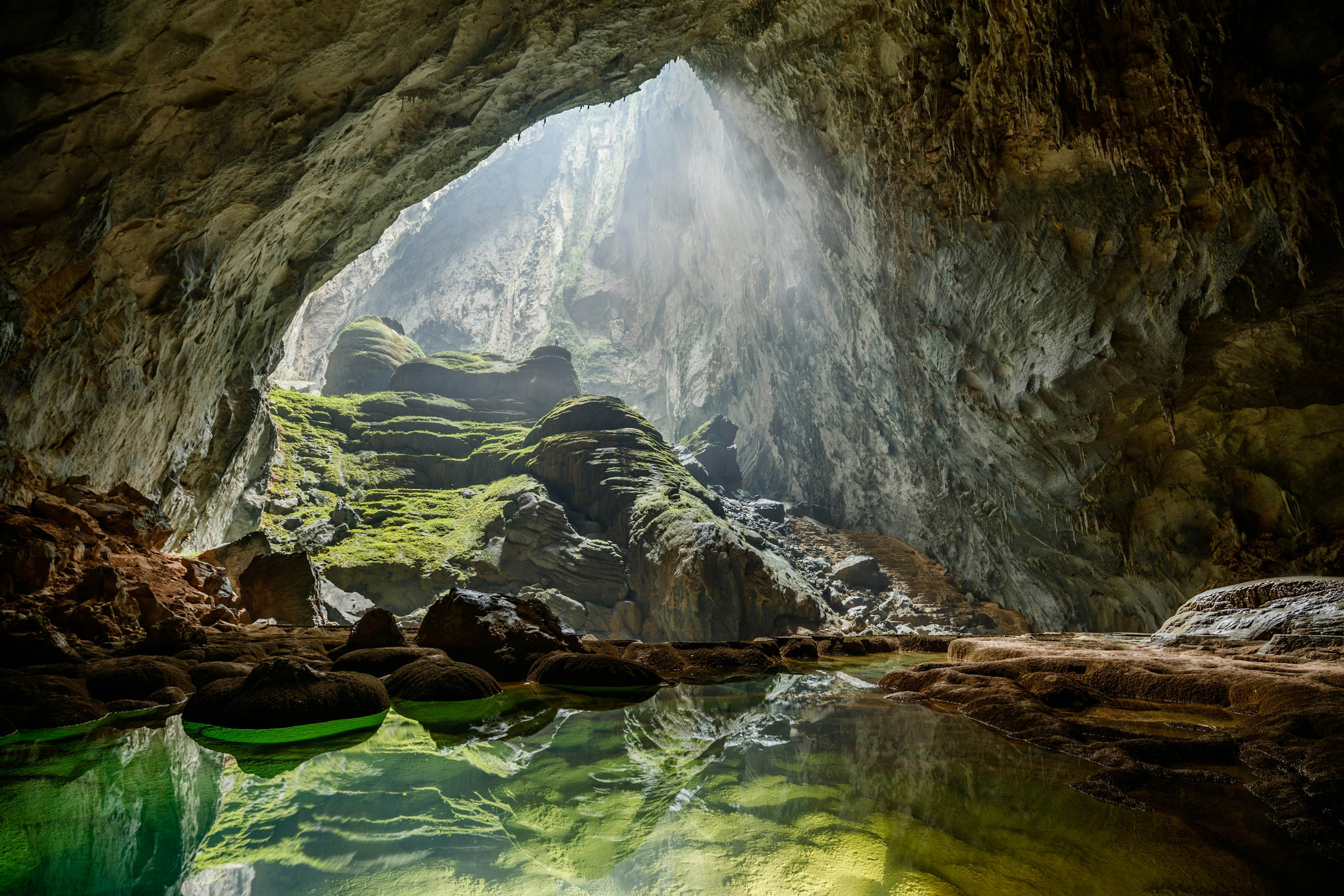 Sunlight shines down through an opening in the cave into a clear green pool of water