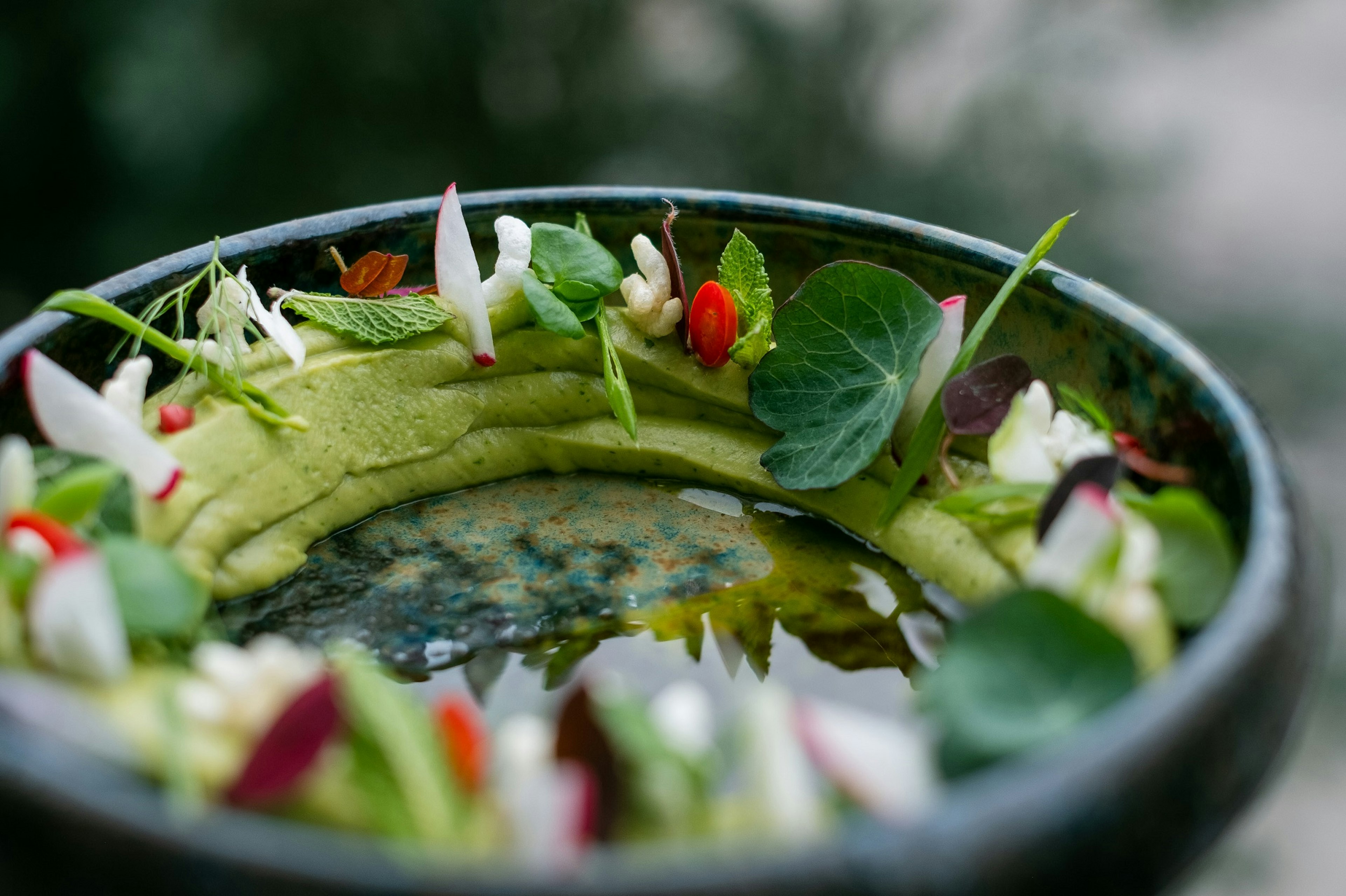 A beautiful blue-green bowl is lined around its edges with guacamole; atop the guacamole are sliced bits of beetroot, mint and other trimmings.